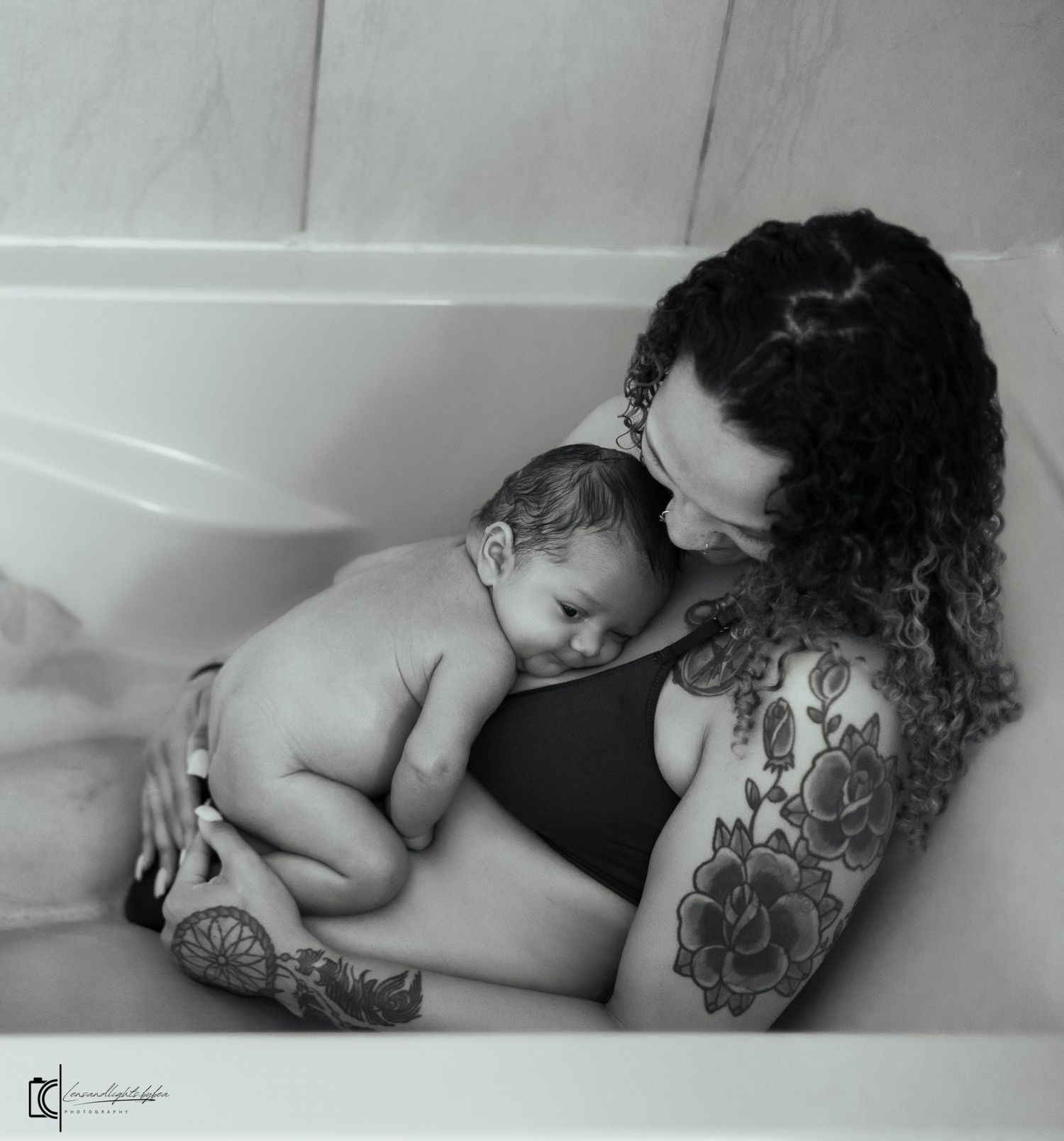 Black and white photograph of a tender moment between parent and sleeping infant with visible tattoo artwork.