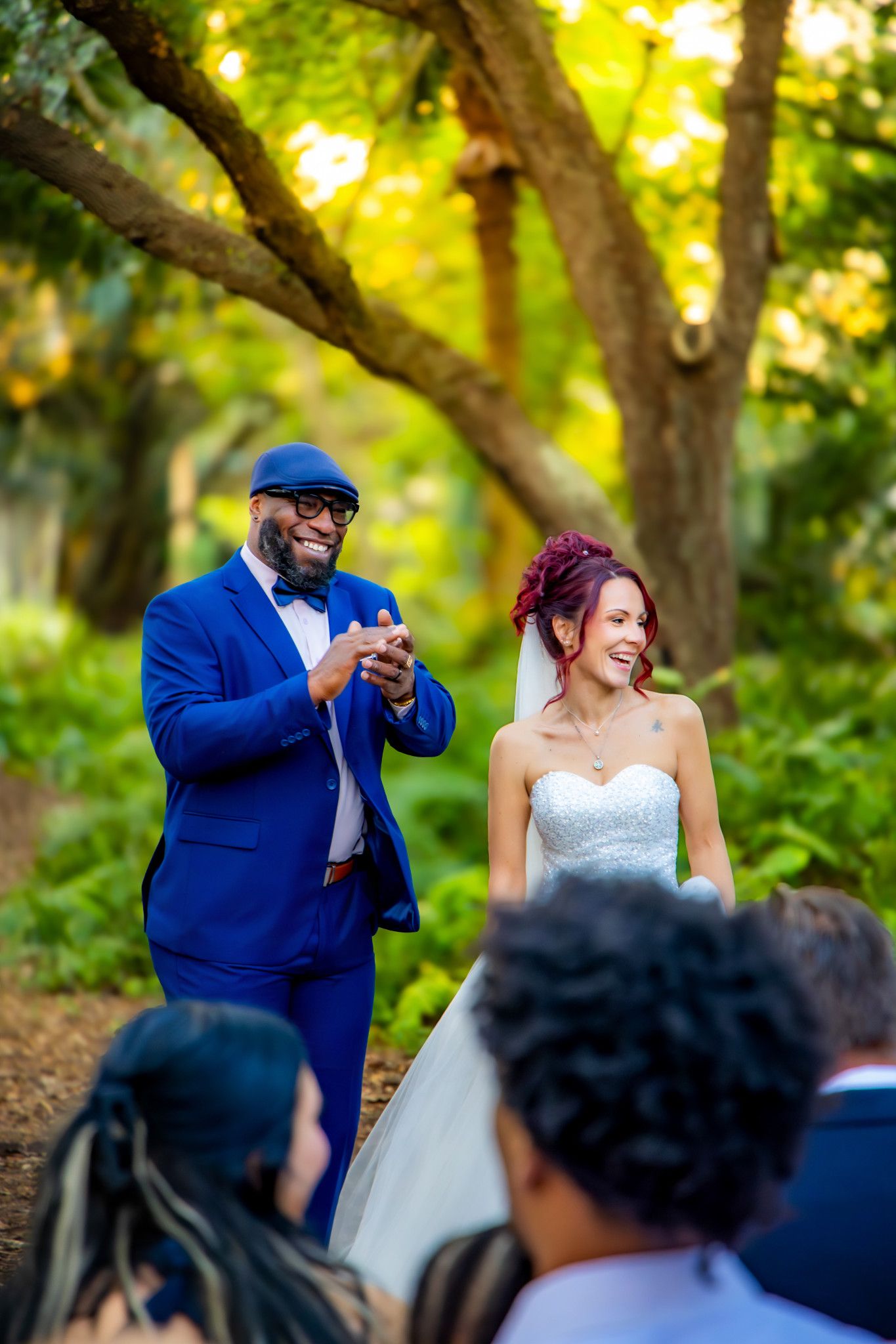 A joyful wedding ceremony moment captured in a sunlit outdoor garden setting with vibrant yellow-green foliage.