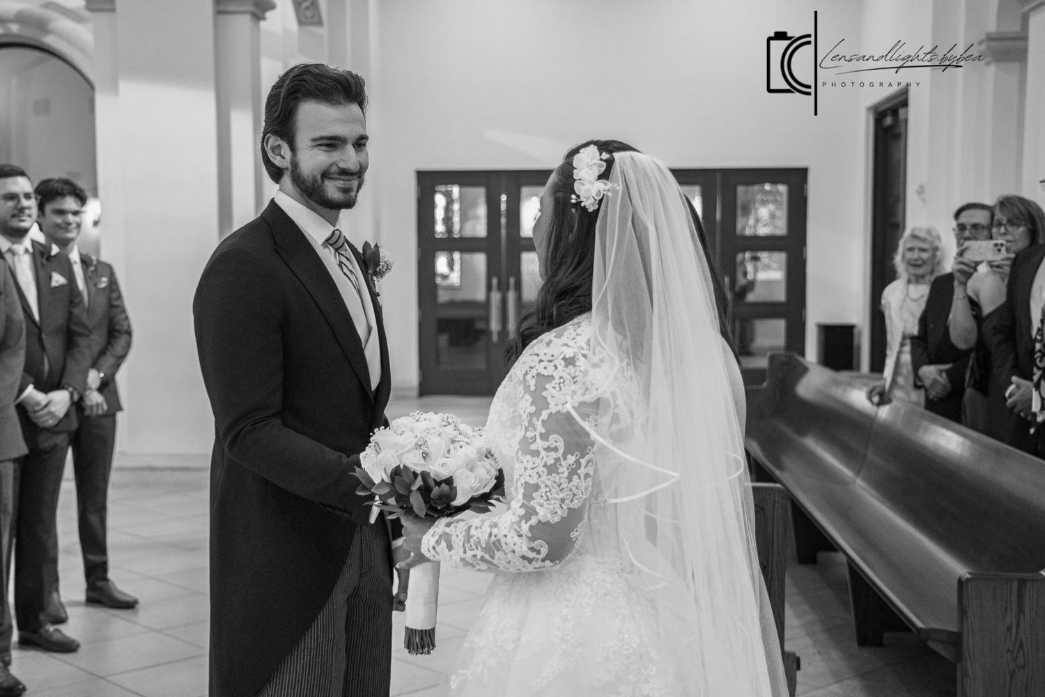 Black and white wedding photo of bride and groom exchanging vows at church altar with guests watching.