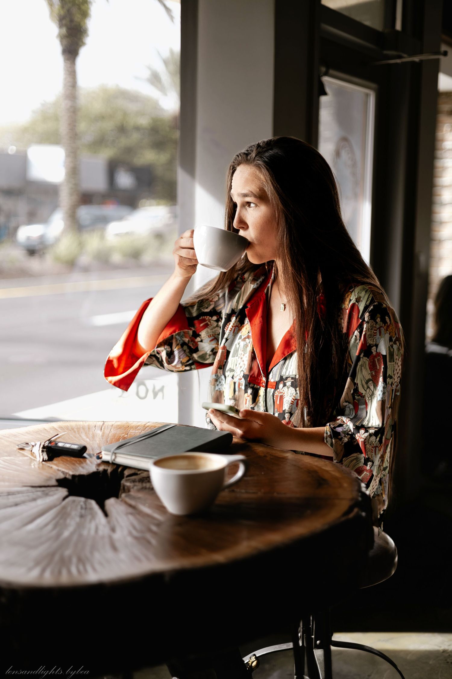 Person enjoying coffee while reading at wooden table in dimly lit cafe.