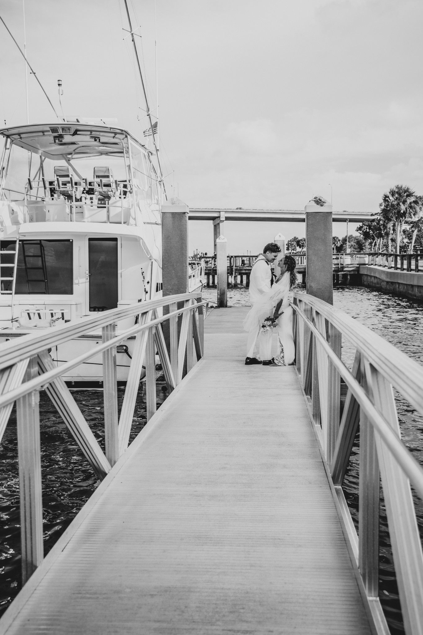 Couple sharing a romantic kiss on a marina dock beside a yacht in black and white photography.