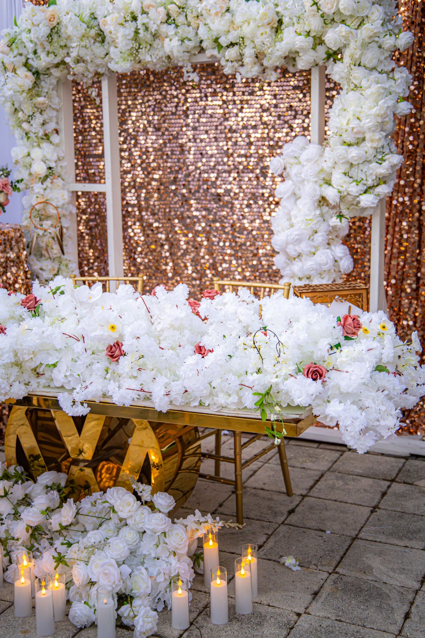Romantic wedding ceremony setup with white floral wall decorations, glowing candles, and rustic brick backdrop.