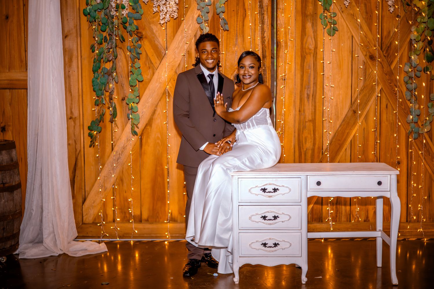 A romantic wedding reception scene with twinkle lights and greenery decorating a rustic wooden barn interior.