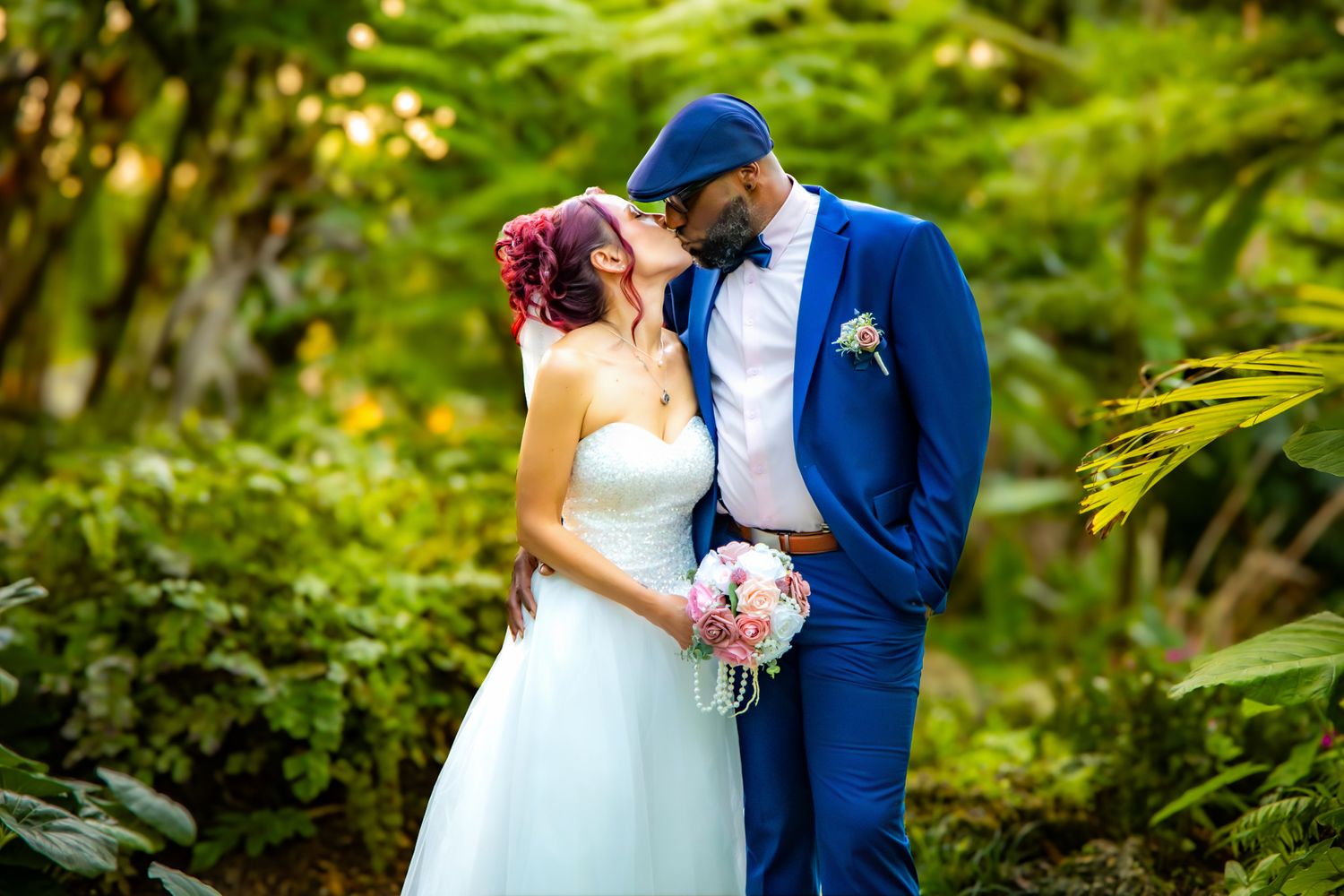 A couple in wedding attire embraces in a lush green garden setting with soft natural lighting.