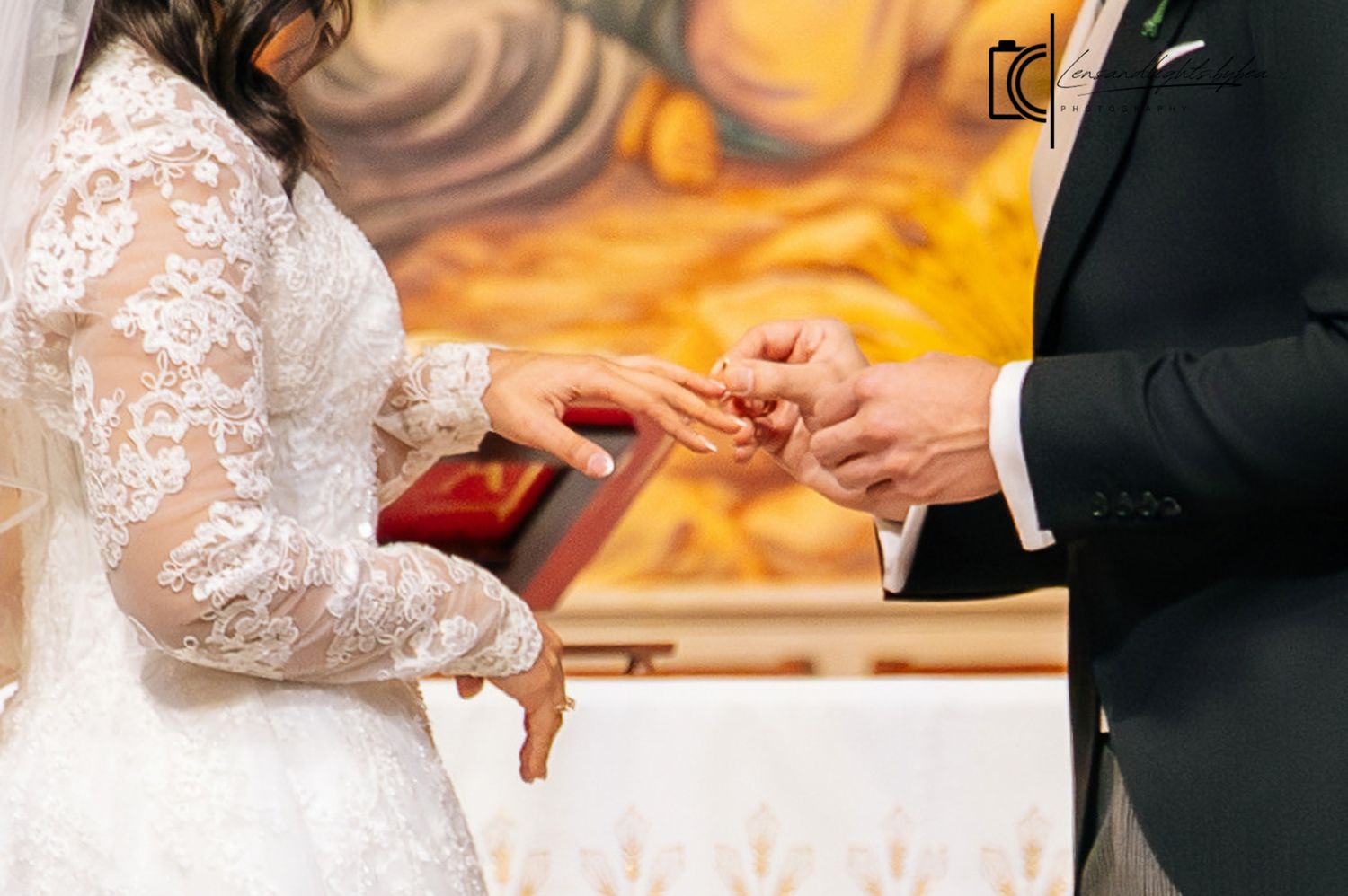 Bride in lace wedding gown receives gold ring from groom during church wedding ceremony.