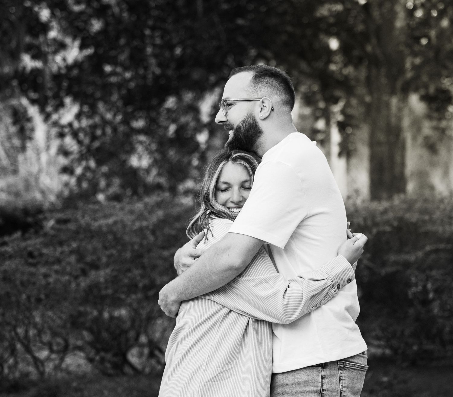 A series of black and white photographs showing tender moments of a couple embracing outdoors in a garden setting.