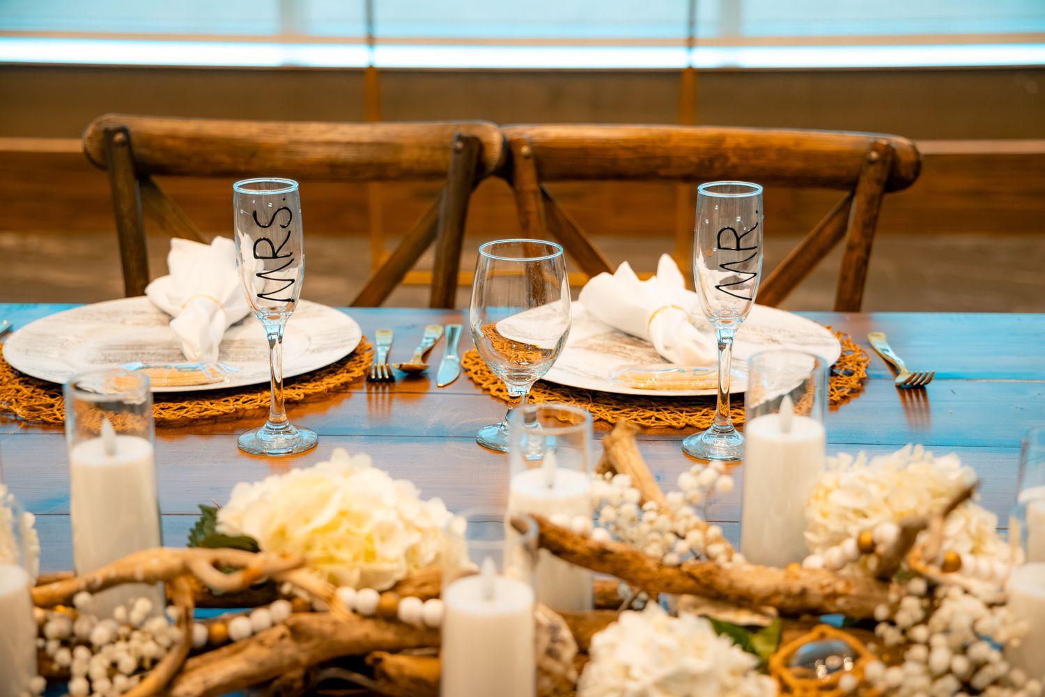 Elegant wedding table setting with MRS and MR champagne flutes, white floral centerpiece, candles, and gold charger plates.