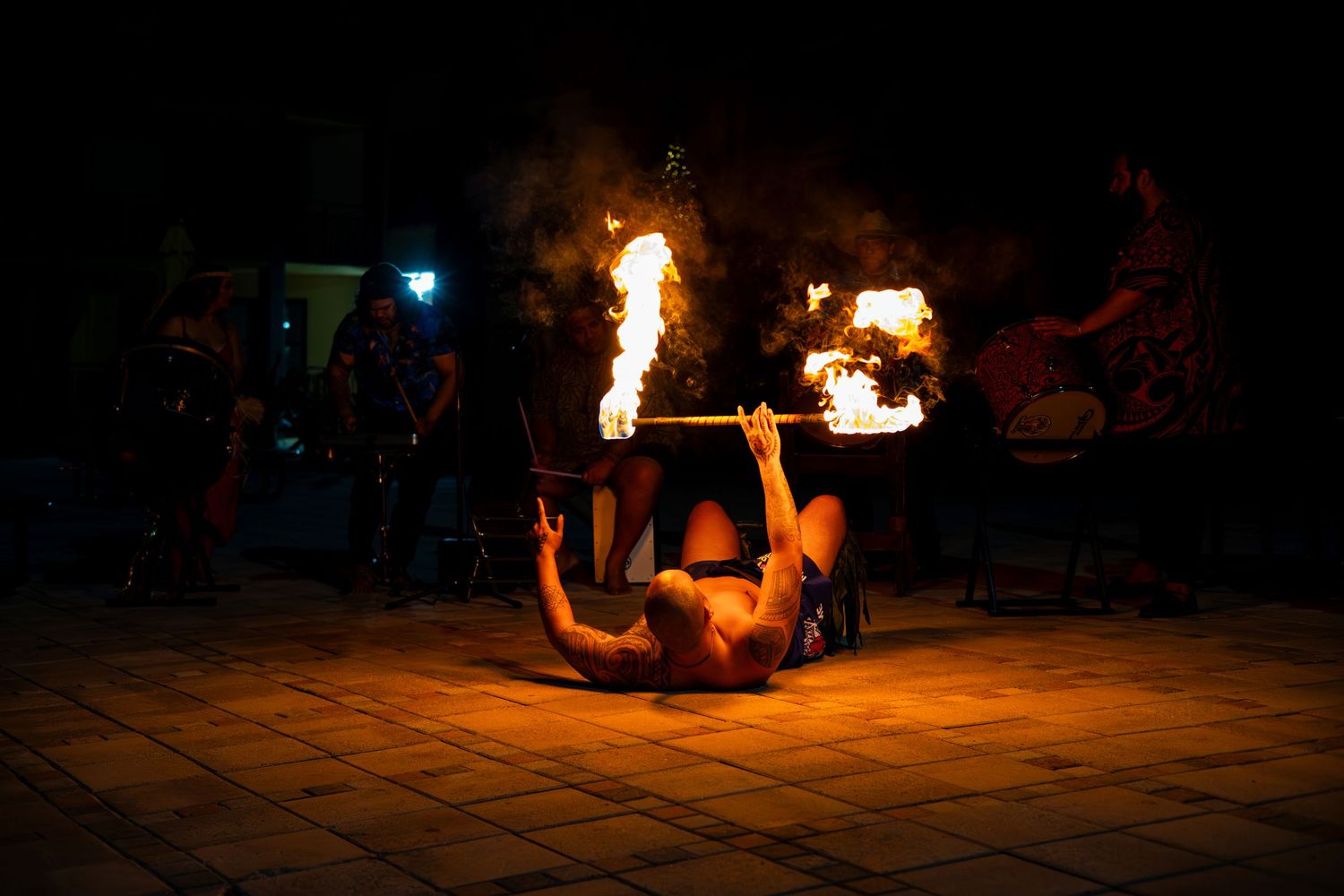 Fire performer spinning flaming batons in a dark outdoor setting creating circular patterns of light and sparks.