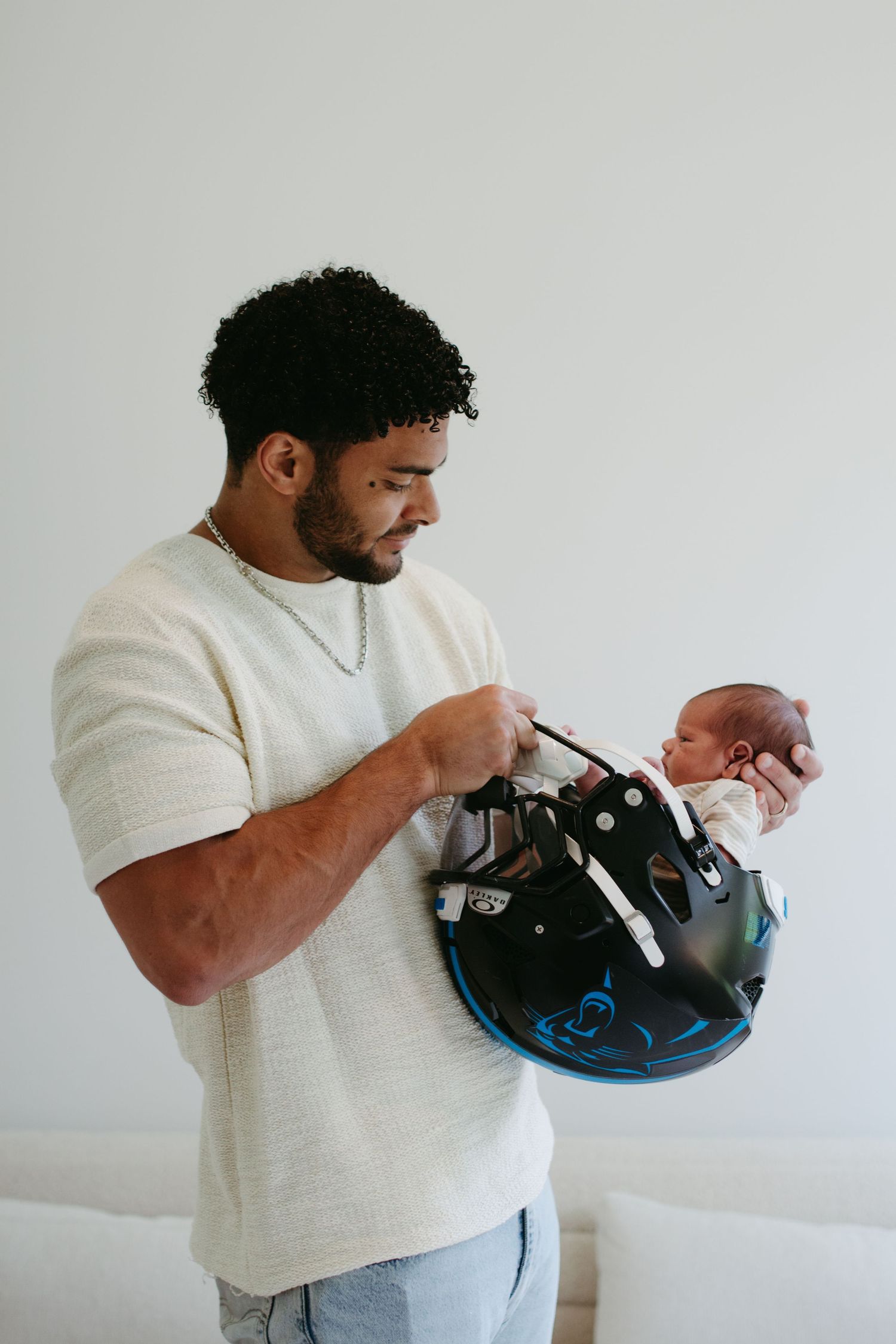 NFL Carolina Panthers player holding newborn in his football helmet during a newborn photography session