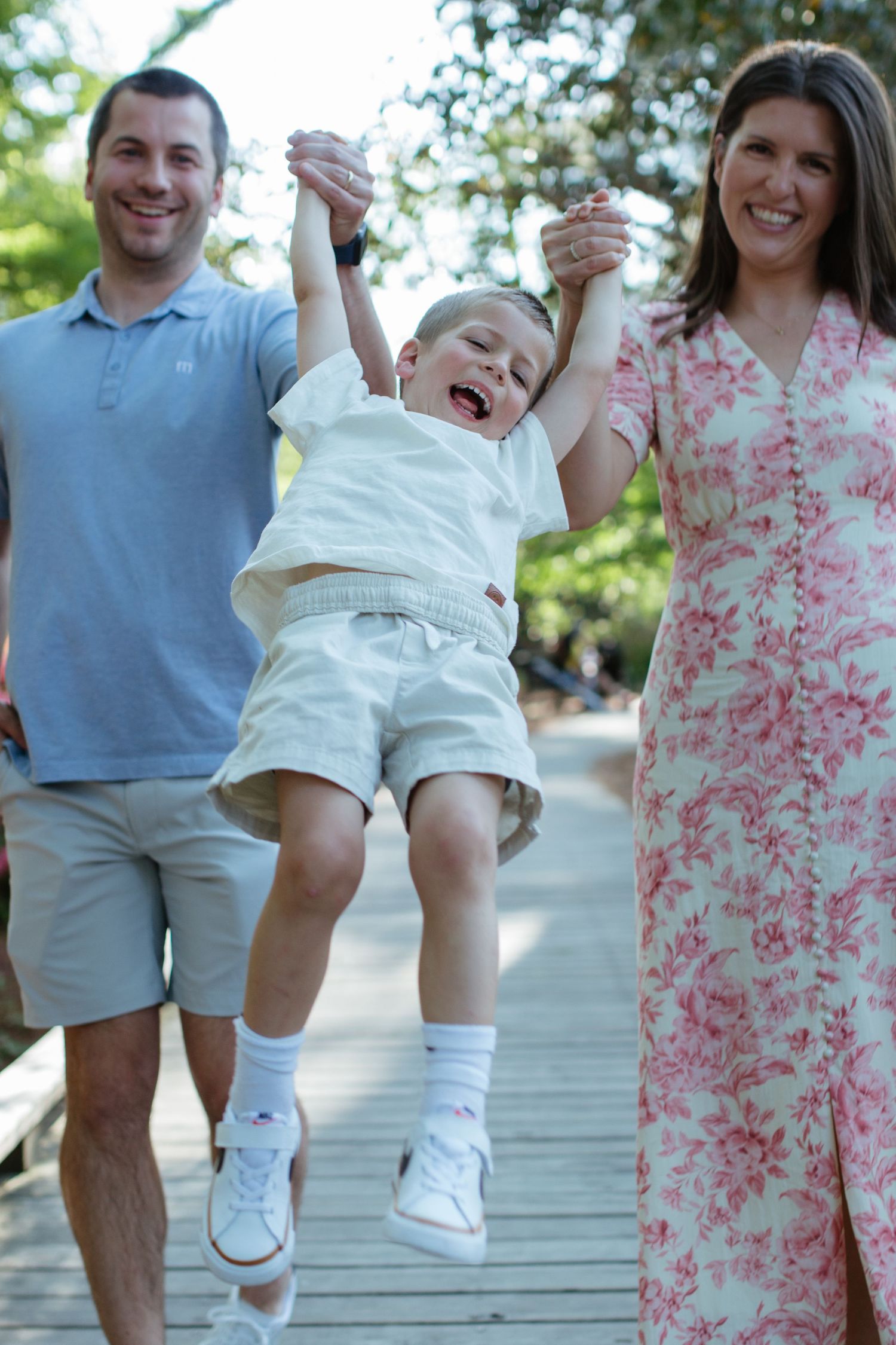 Family swinging young laughing child between them on wooden boardwalk, outdoor summer day at glencairn gardens