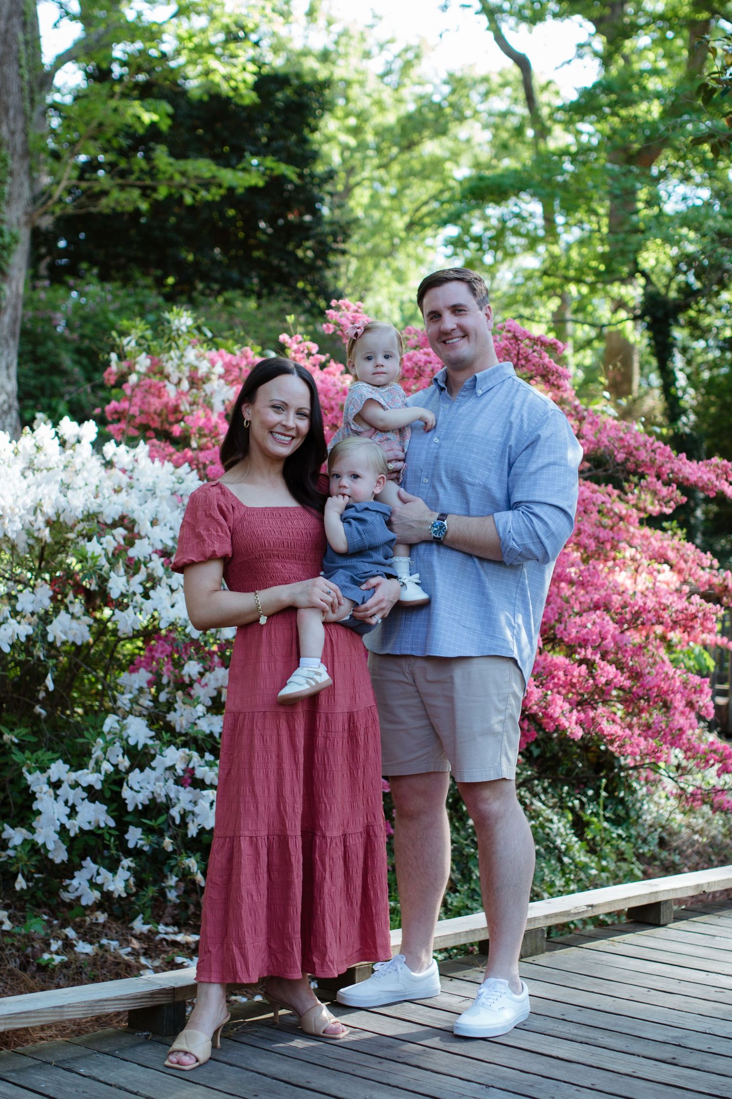 Family of four poses on a wooden bridge surrounded by blooming pink and white azaleas in a lush gardenin rock hill