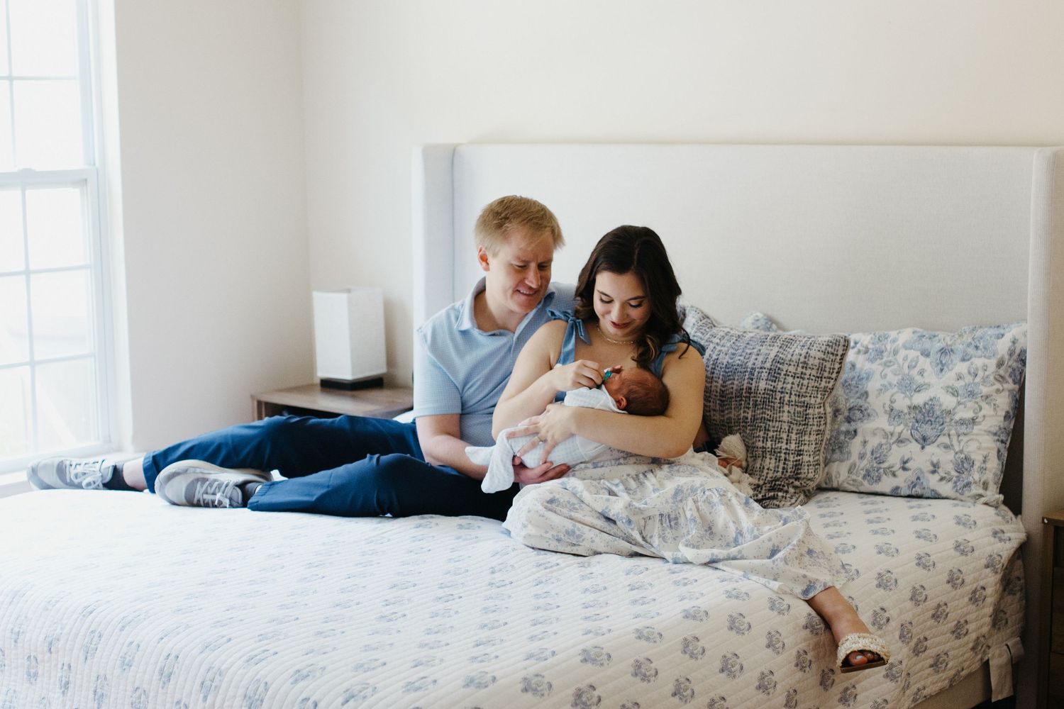 parents sitting on bed in their bedroom holding their newborn baby in their arms at in-home newborn session