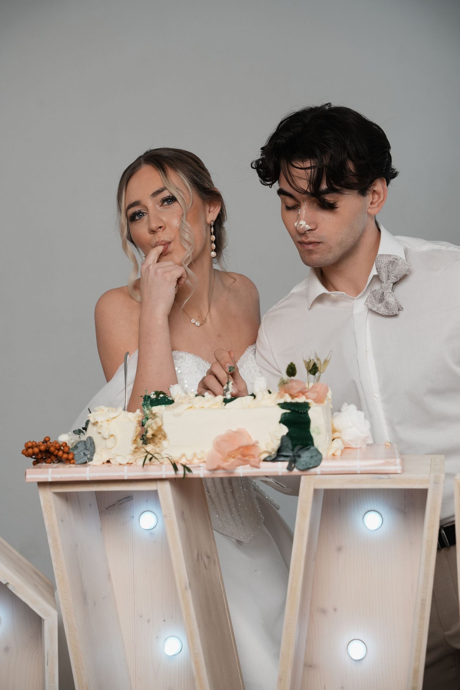 Bride and groom cutting their wedding cake decorated with flowers on an illuminated table.