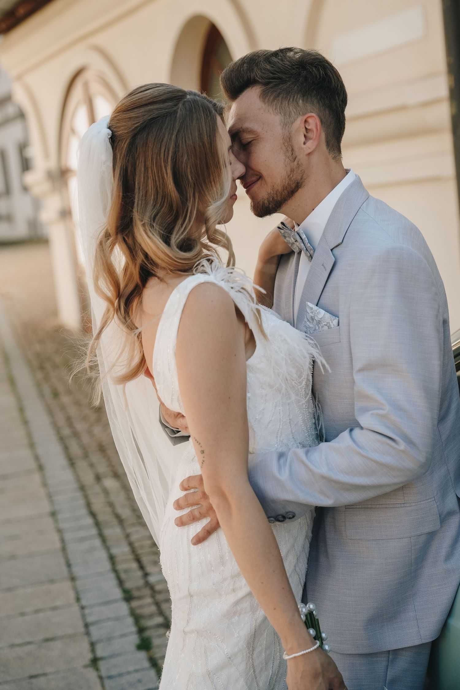 A bride and groom share a romantic moment, nearly kissing outdoors near a classic building on their wedding day.