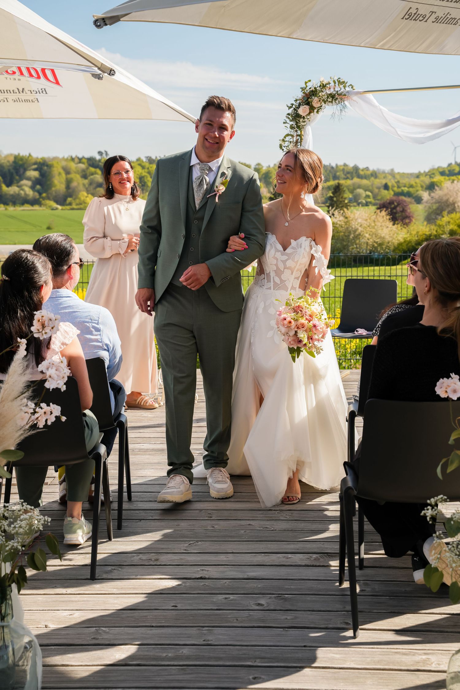 Bride and groom walk down the aisle at an outdoor wedding ceremony on a sunny day.