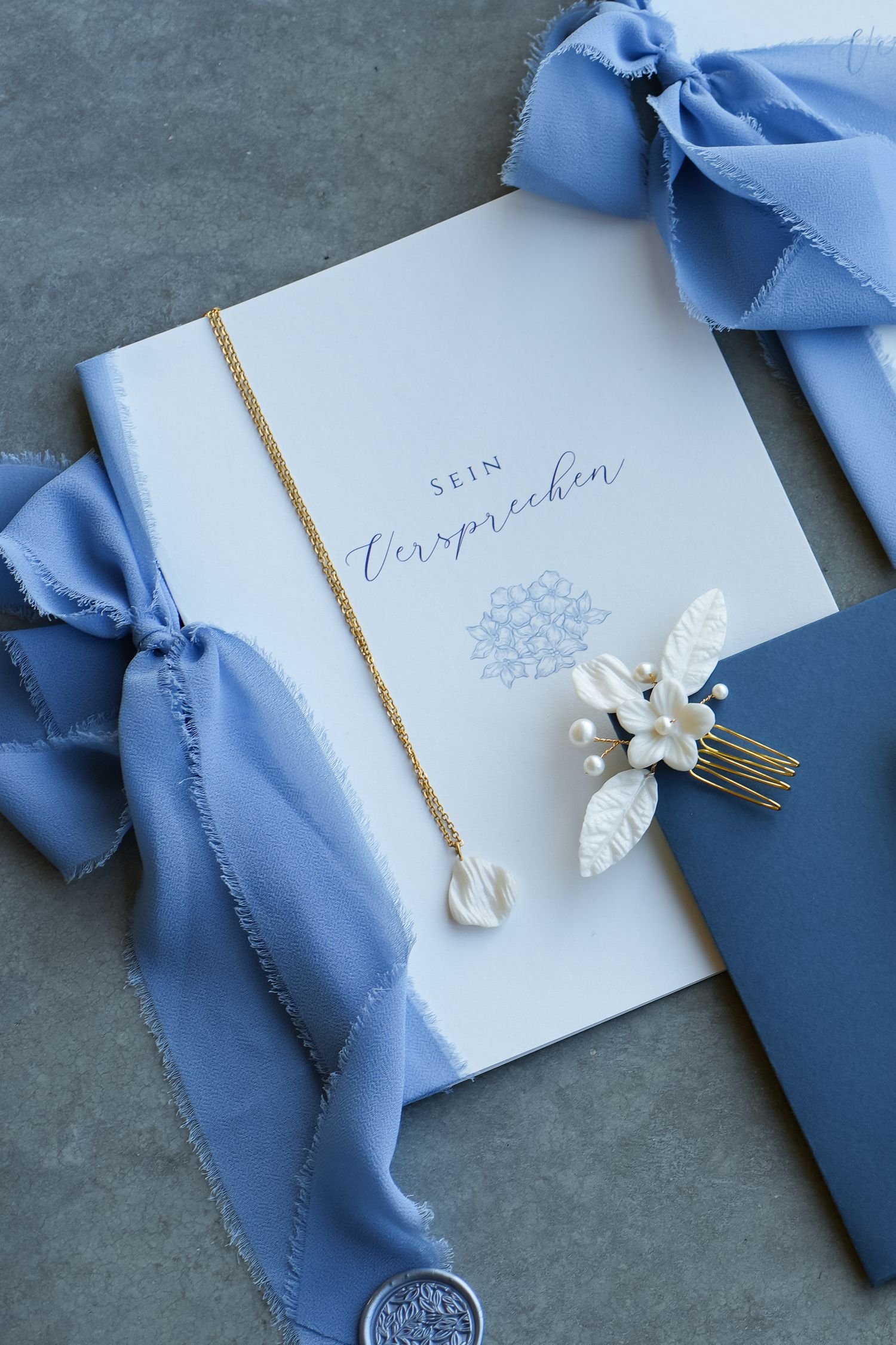 Elegant wedding stationery with blue ribbon, gold necklace, pearl hair comb, and 