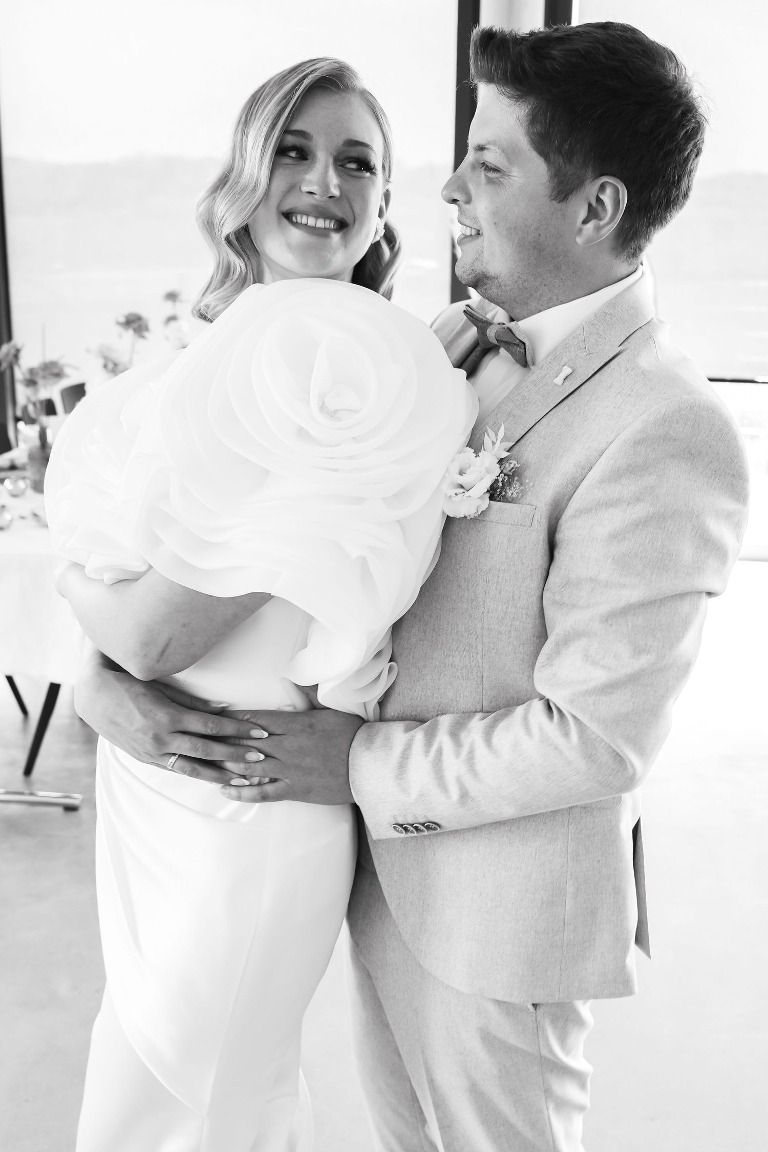 Black and white photo of a smiling bride and groom embracing at their wedding reception.