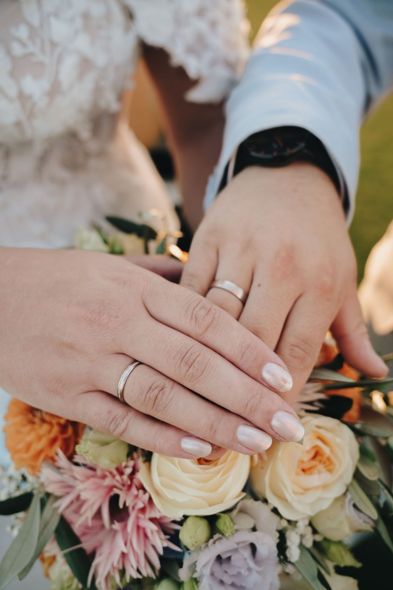 Newlyweds displaying wedding rings on hands resting over a colorful bridal bouquet with roses.