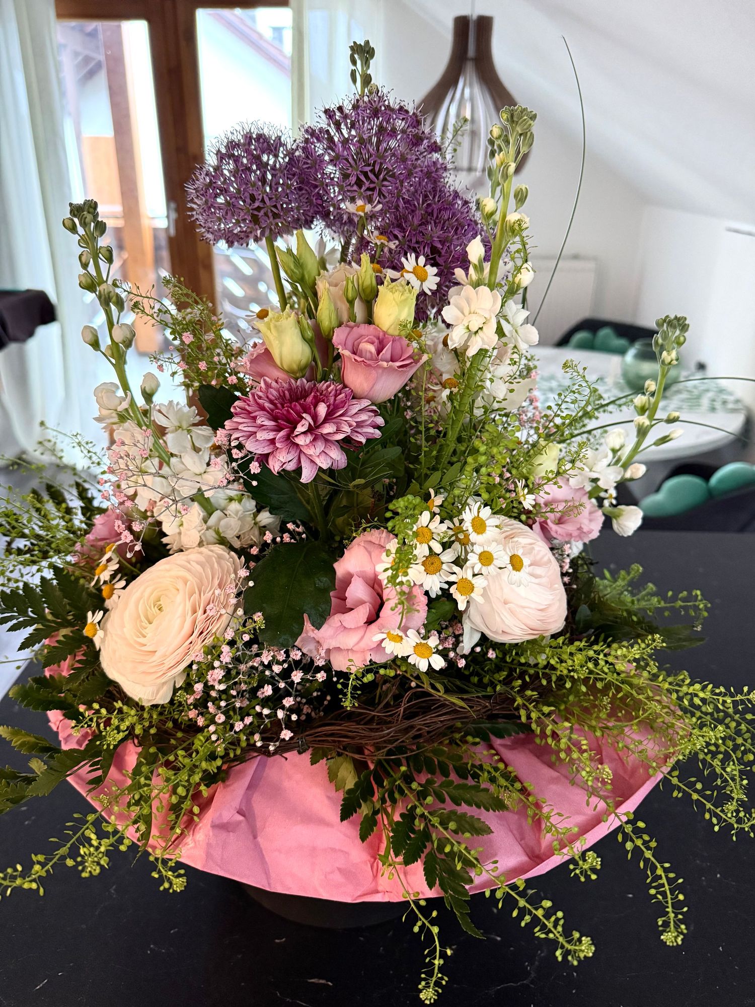 Beautiful mixed floral arrangement with pink roses, purple allium, daisies, and chrysanthemums in a pink wrapped vase.