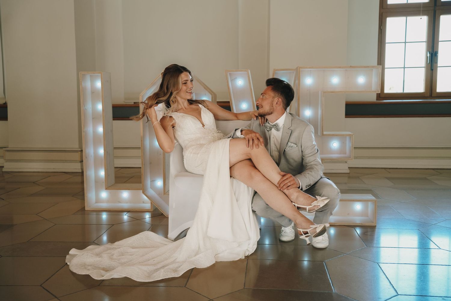 Bride and groom posing elegantly in front of illuminated LOVE letters at a romantic wedding venue.
