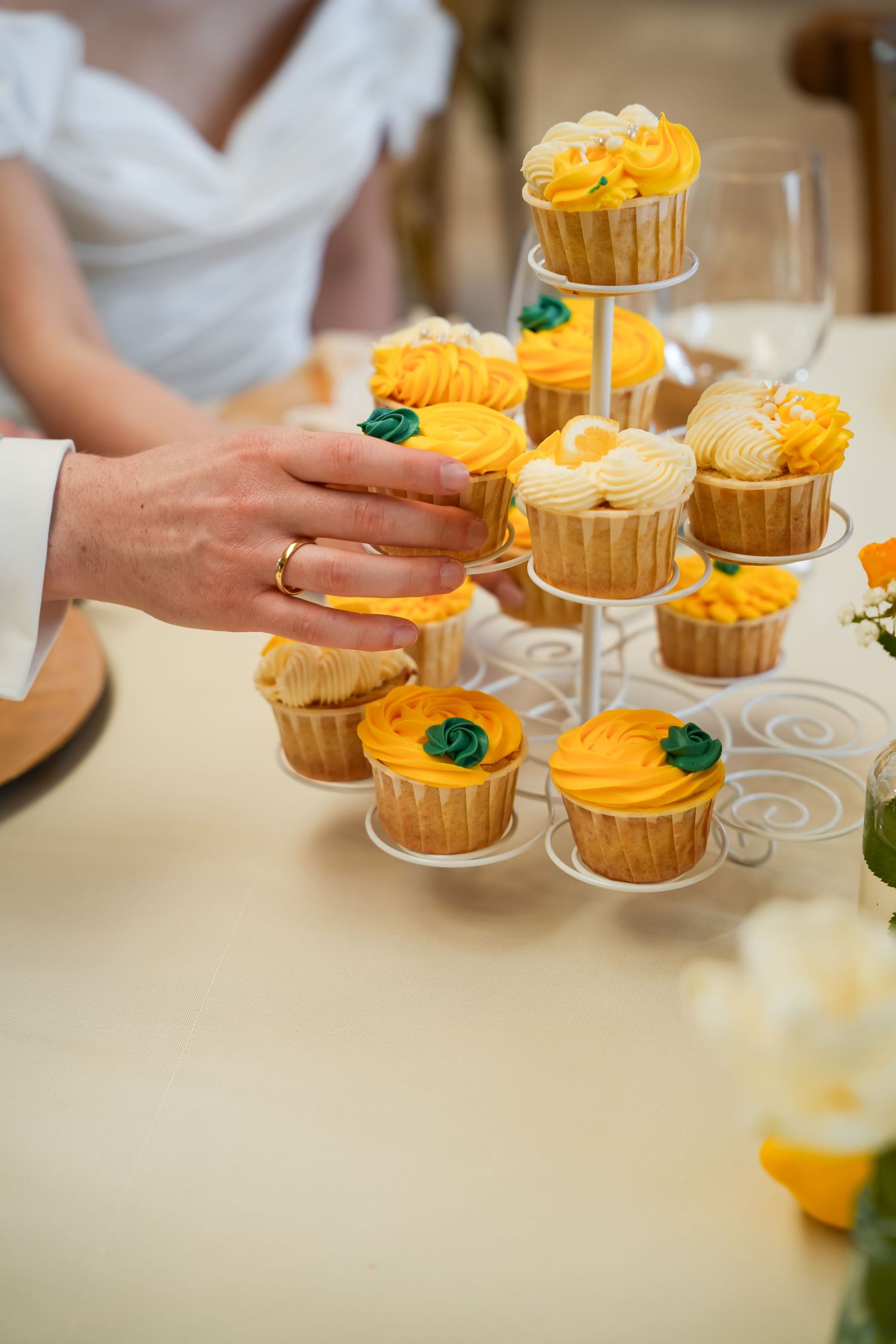 Bride and groom picking yellow frosted cupcakes from a tiered white wedding cupcake stand.