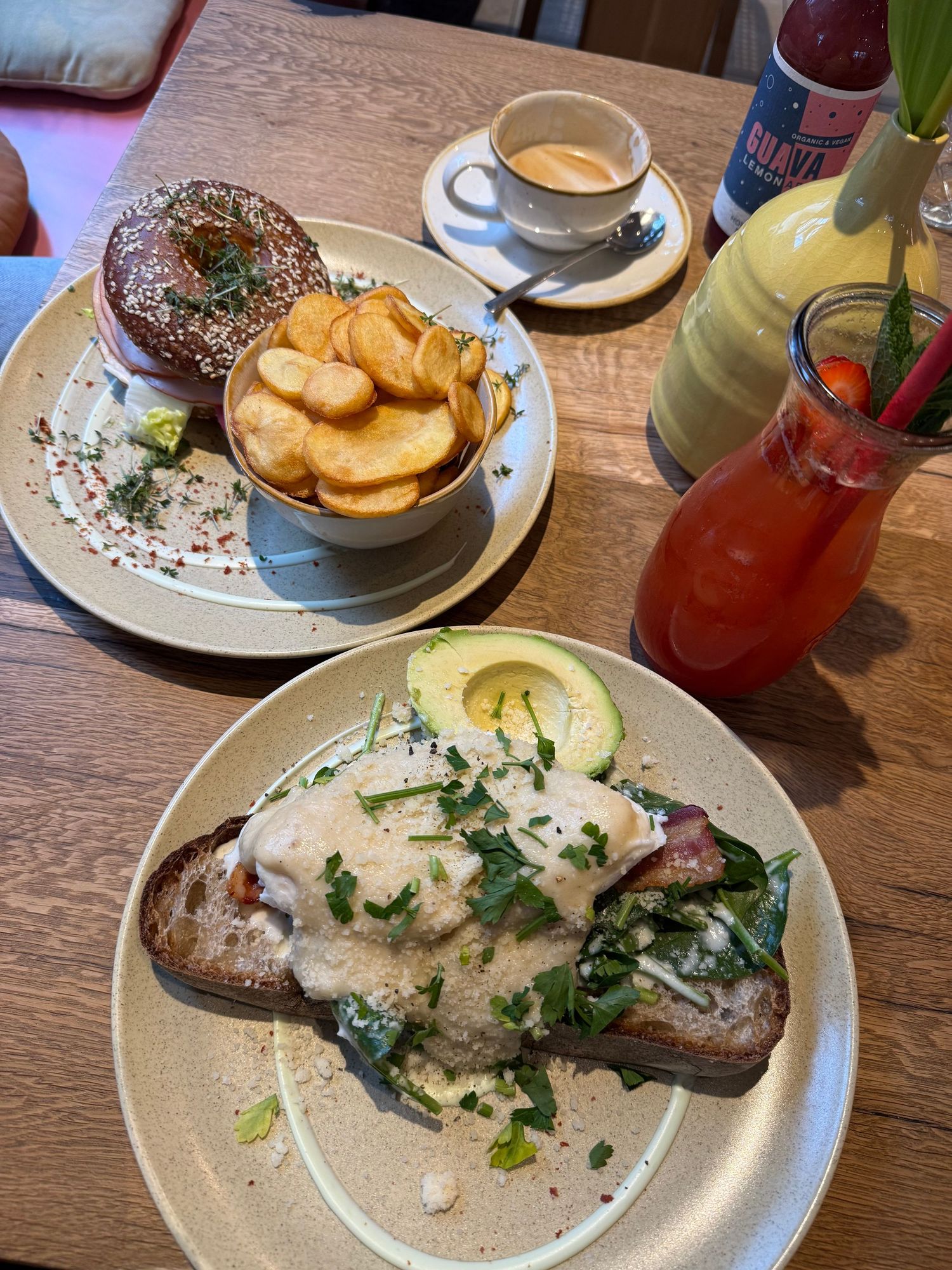 Brunch spread with avocado toast topped with poached eggs, a bagel sandwich with chips, espresso, and a Bloody Mary cocktail.