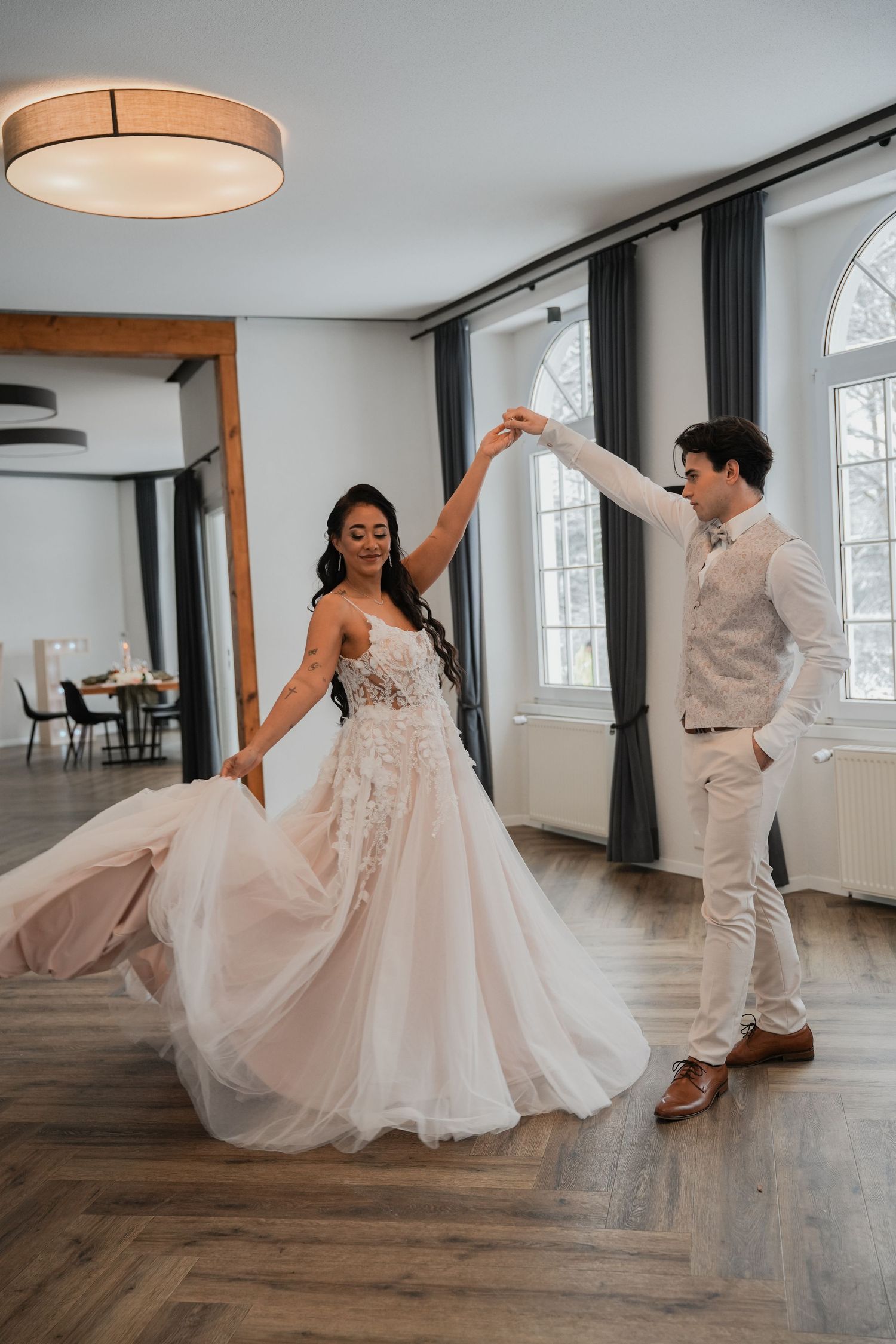 A couple dances together in an elegant room with arched windows and hardwood floors.