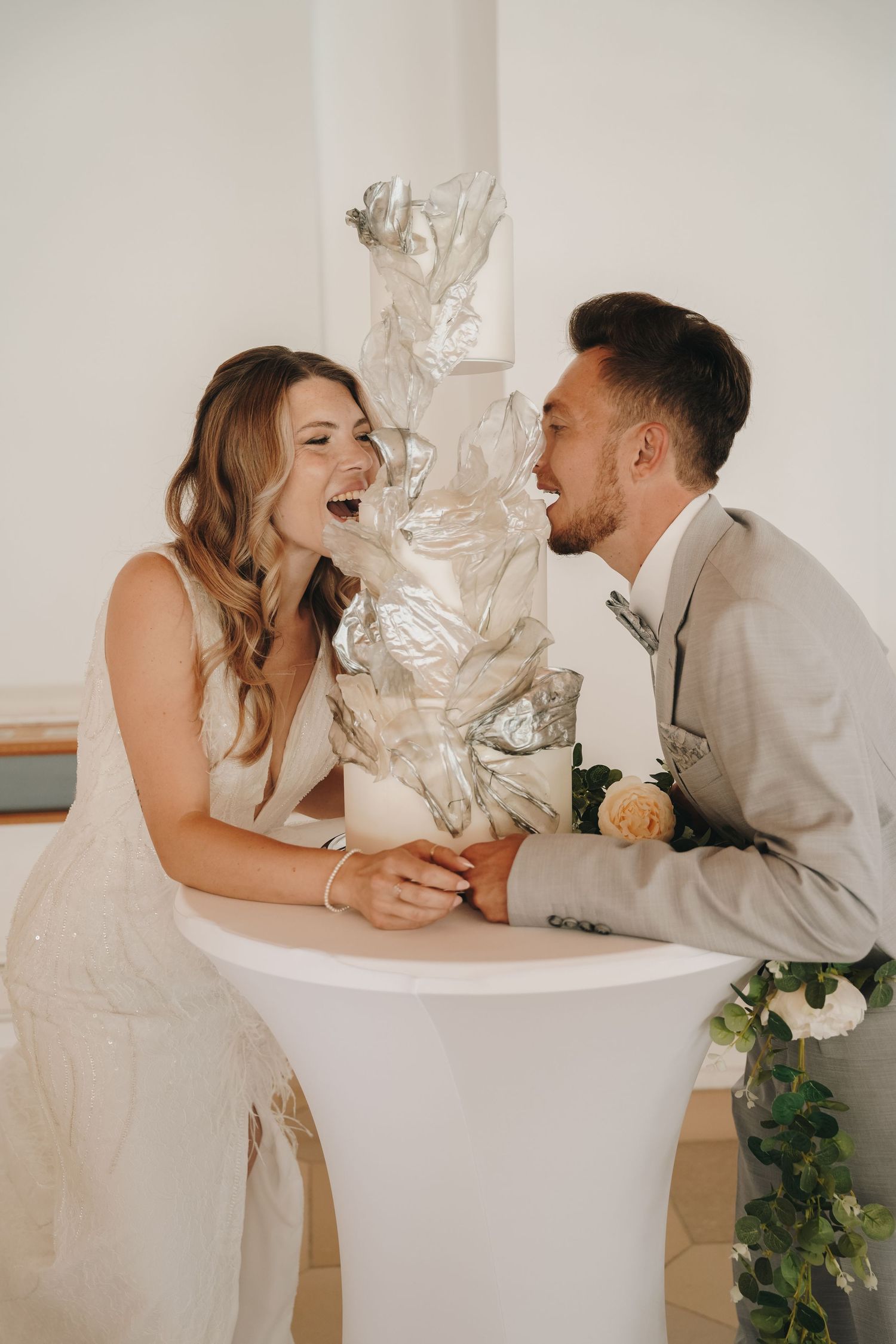 Laughing bride and groom leaning on a white cocktail table at their wedding reception.