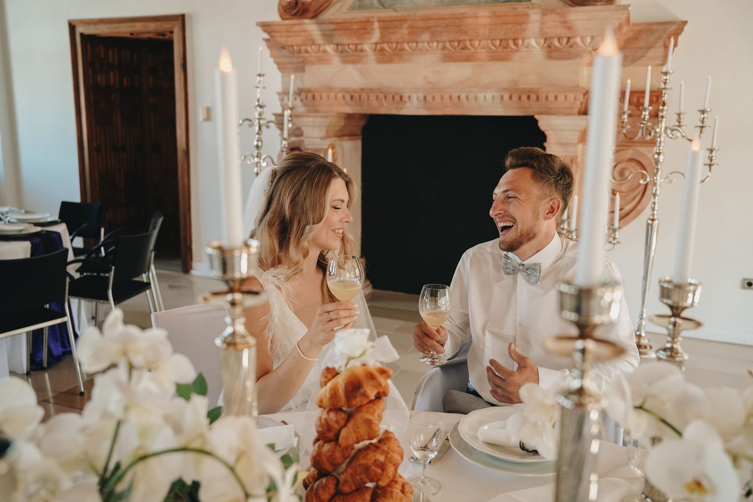 A joyful bride and groom laugh together at their elegant wedding reception table with candles and floral decor.