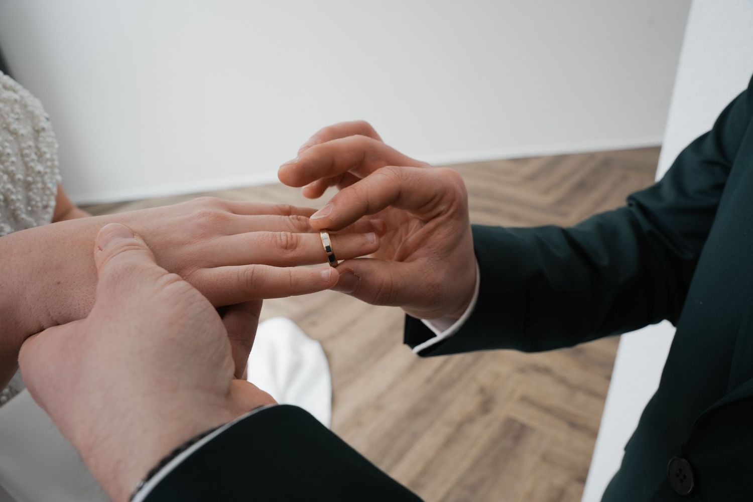 Groom placing a gold wedding ring on bride's finger during a wedding ceremony.