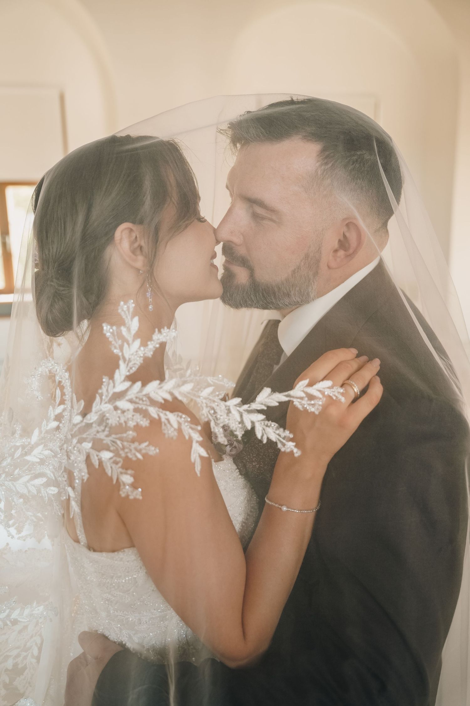 A bride and groom share a romantic kiss under a lace veil on their wedding day.