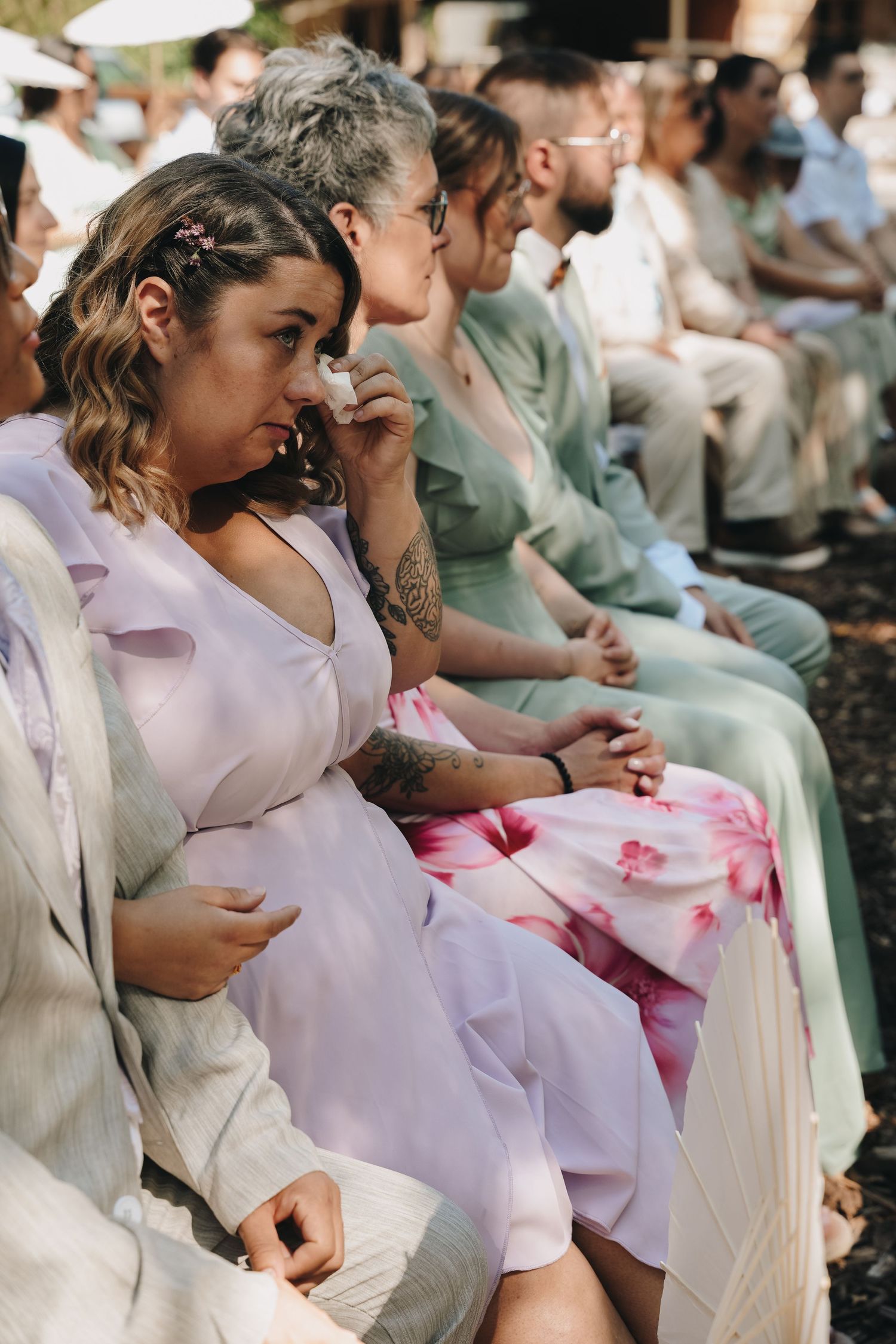 Guests in pastel dresses seated outdoors at an elegant garden wedding ceremony on a sunny day.
