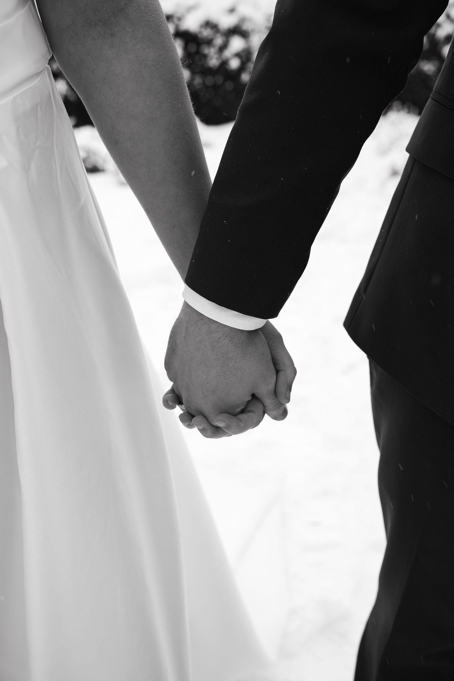Black and white photo of bride and groom holding hands at wedding ceremony, wearing formal attire.