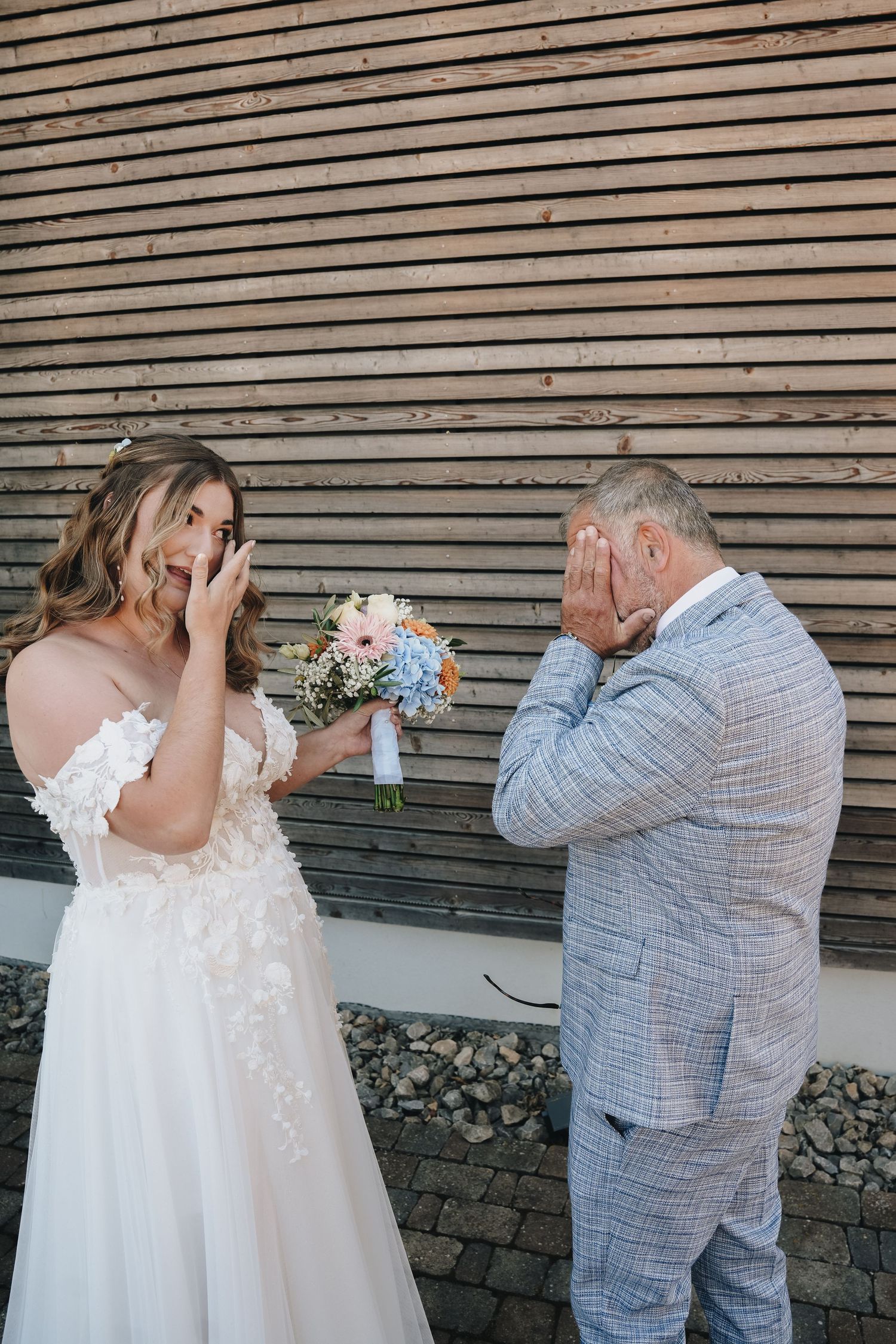 Emotional bride and father crying together during first look moment, bride in white gown holding pastel bouquet.