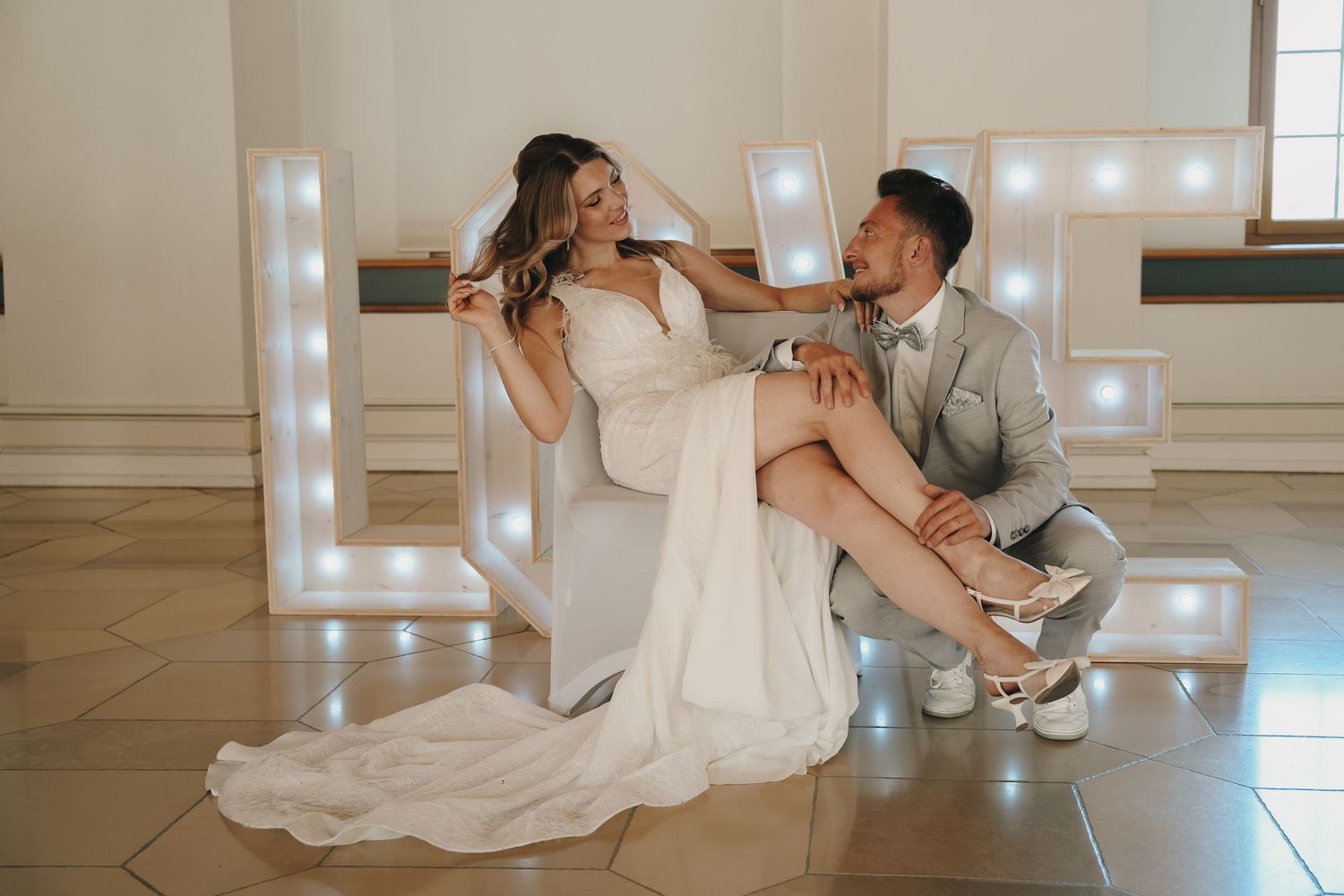 Bride and groom posing elegantly with illuminated LOVE letters at their wedding venue.
