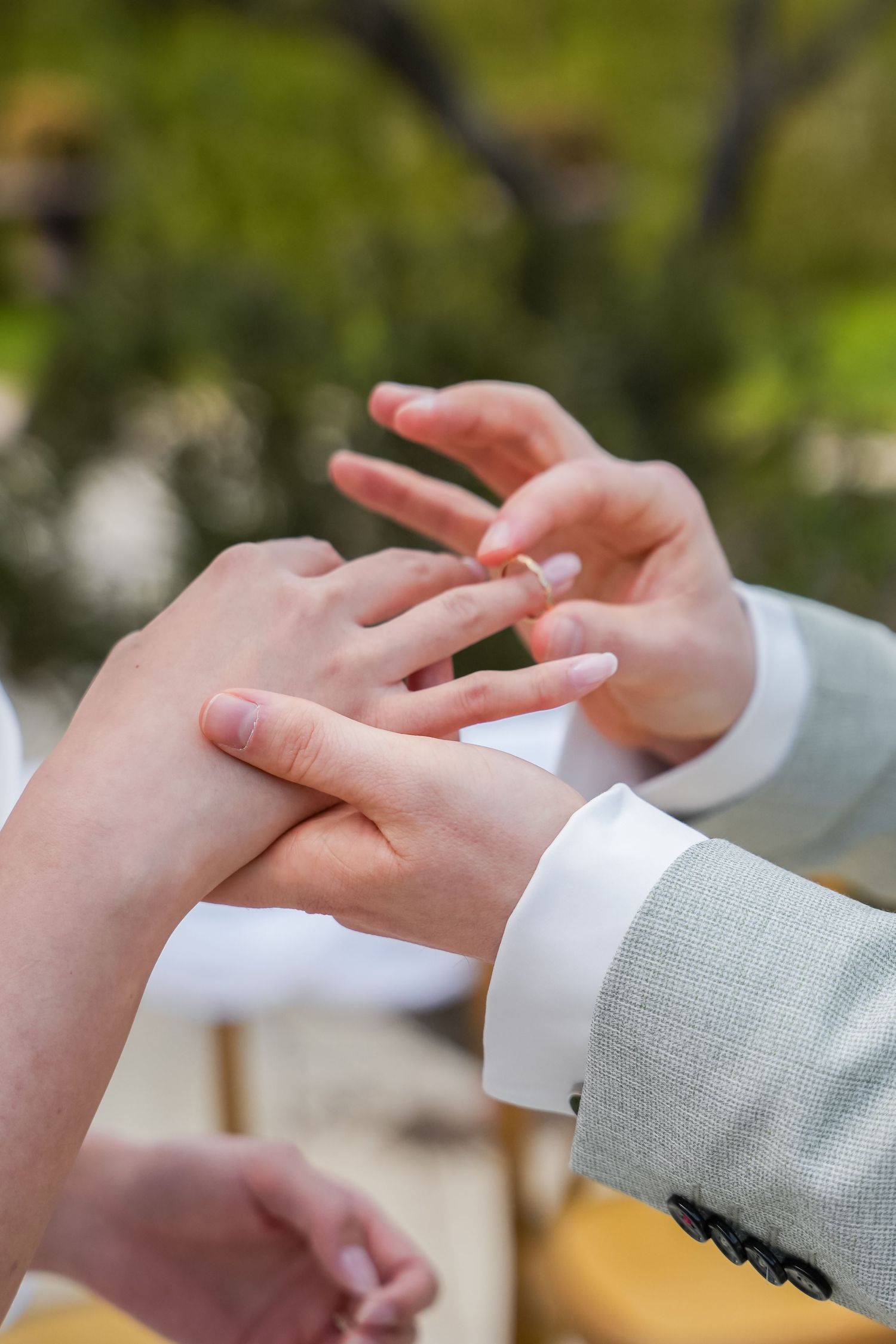 Groom placing a gold wedding ring on bride's finger during an outdoor wedding ceremony.