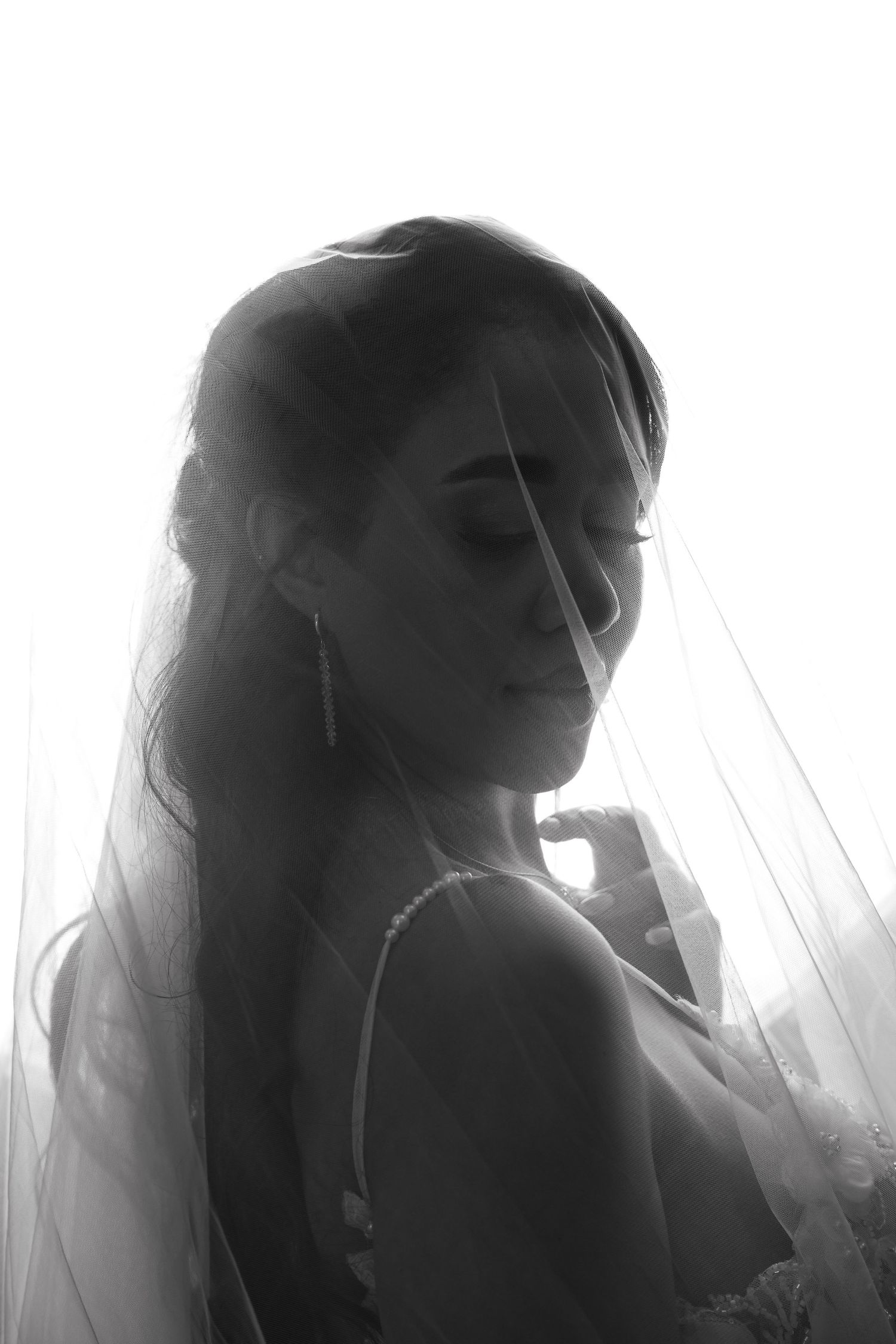 Black and white portrait of a bride wearing a veil, eyes closed, in soft backlit light.
