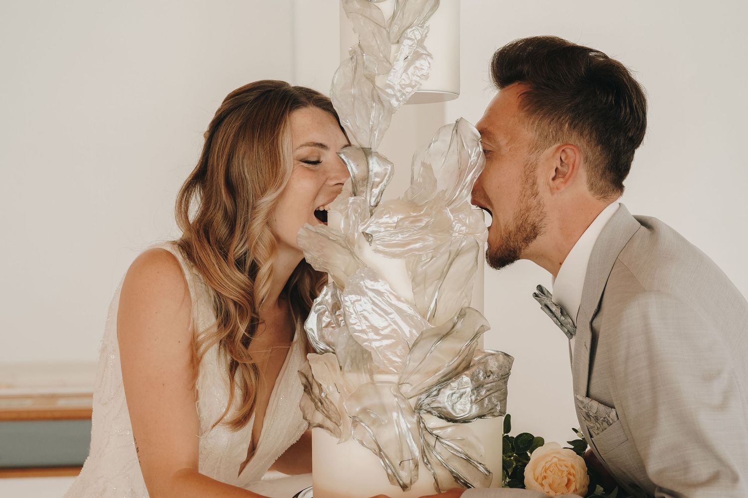 Joyful bride and groom laughing together beside an elegant silver wedding cake on their special day.