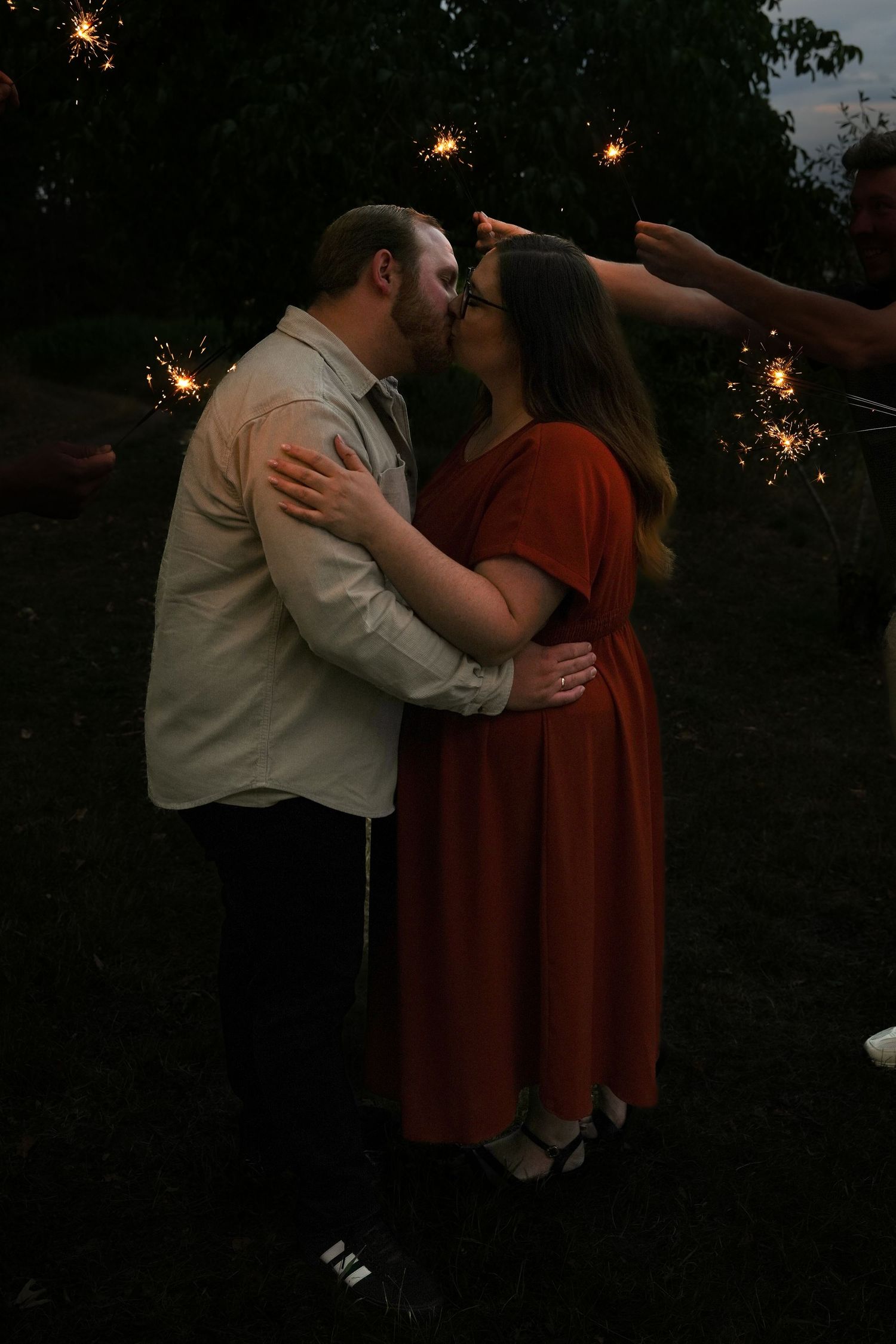 Couple sharing a romantic kiss surrounded by sparkling sparklers at dusk outdoors.