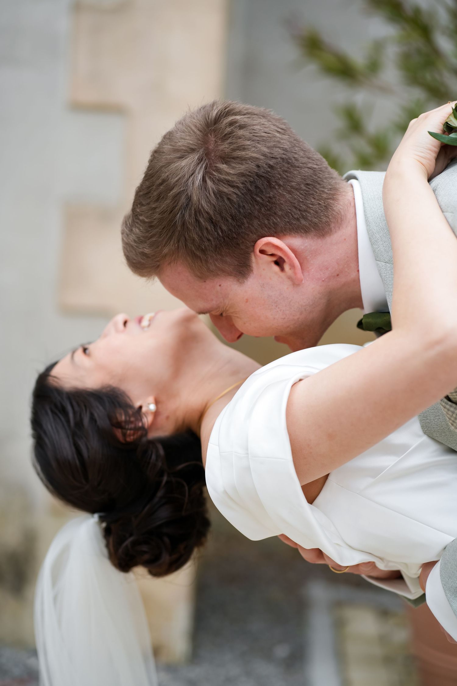 A groom dips his dark-haired bride in a white dress for a romantic kiss during their outdoor wedding ceremony.