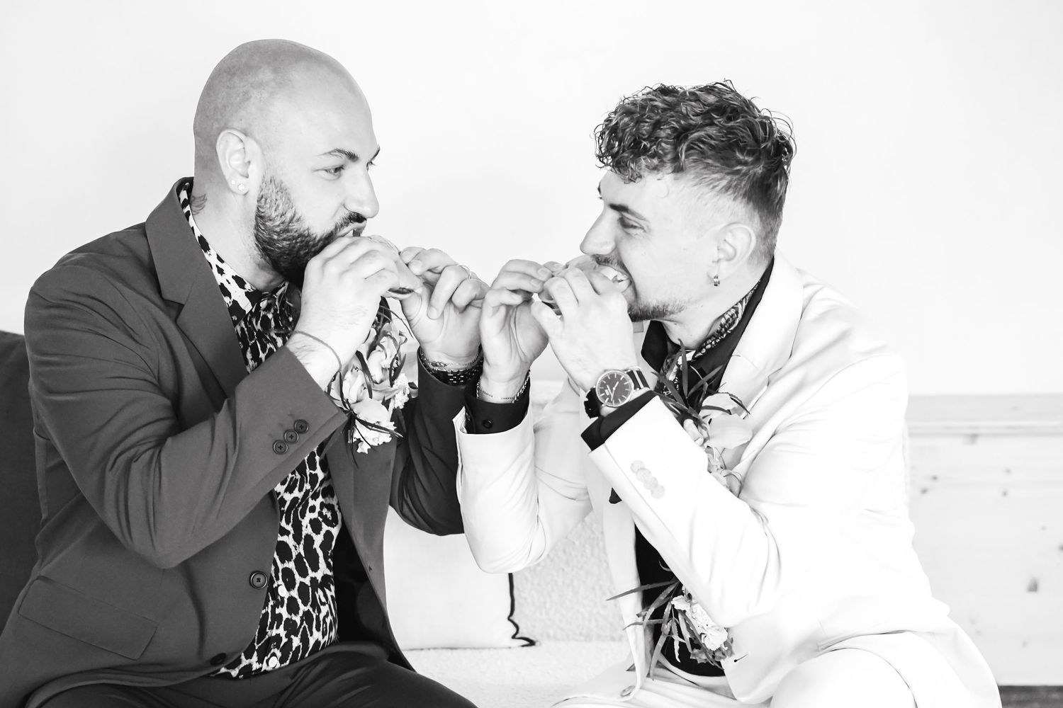 Two men in stylish suits holding hands together in a black and white portrait photo.