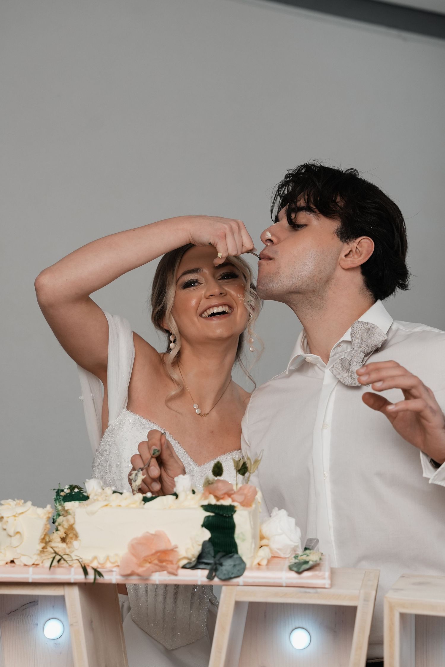 Bride and groom laughing while cutting their white floral wedding cake at their wedding reception.
