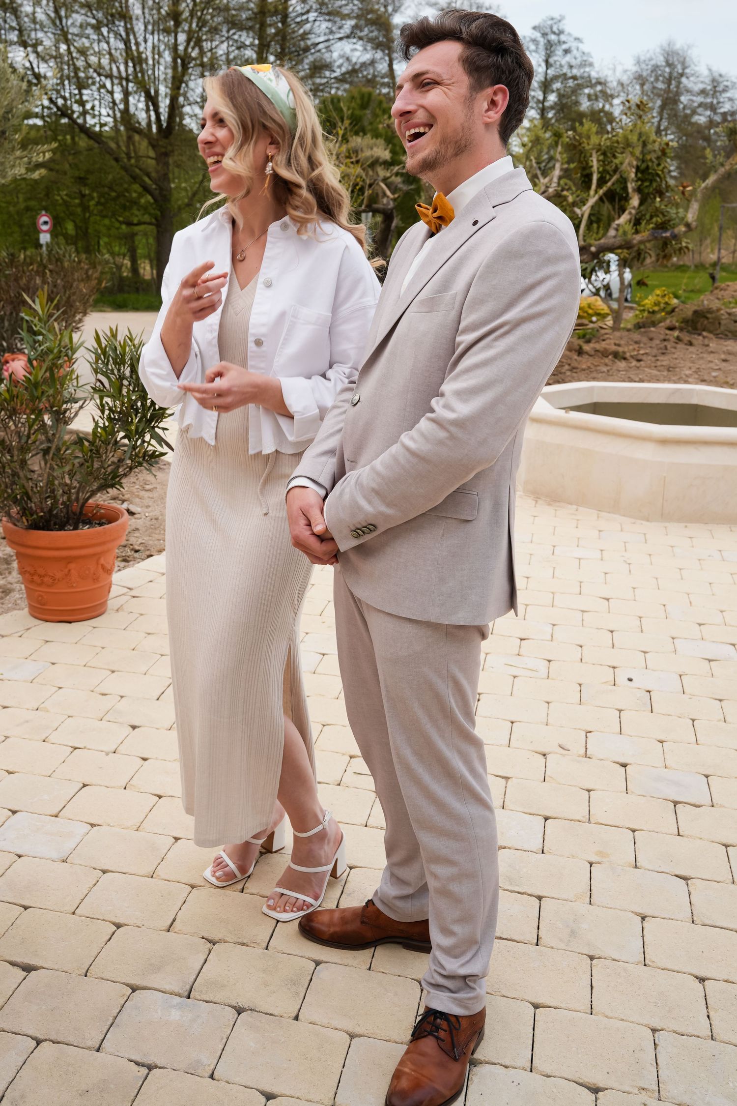 Smiling bride and groom in neutral tones holding hands outdoors on a stone patio at a garden wedding.