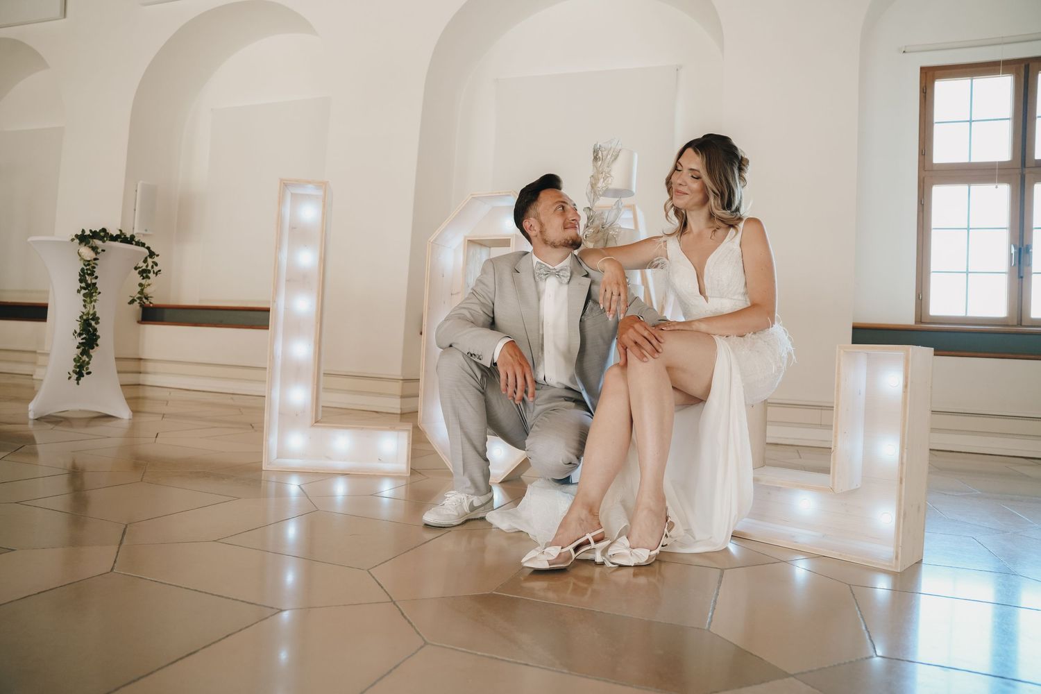 Bride and groom sitting together in front of illuminated marquee letters at elegant wedding venue.