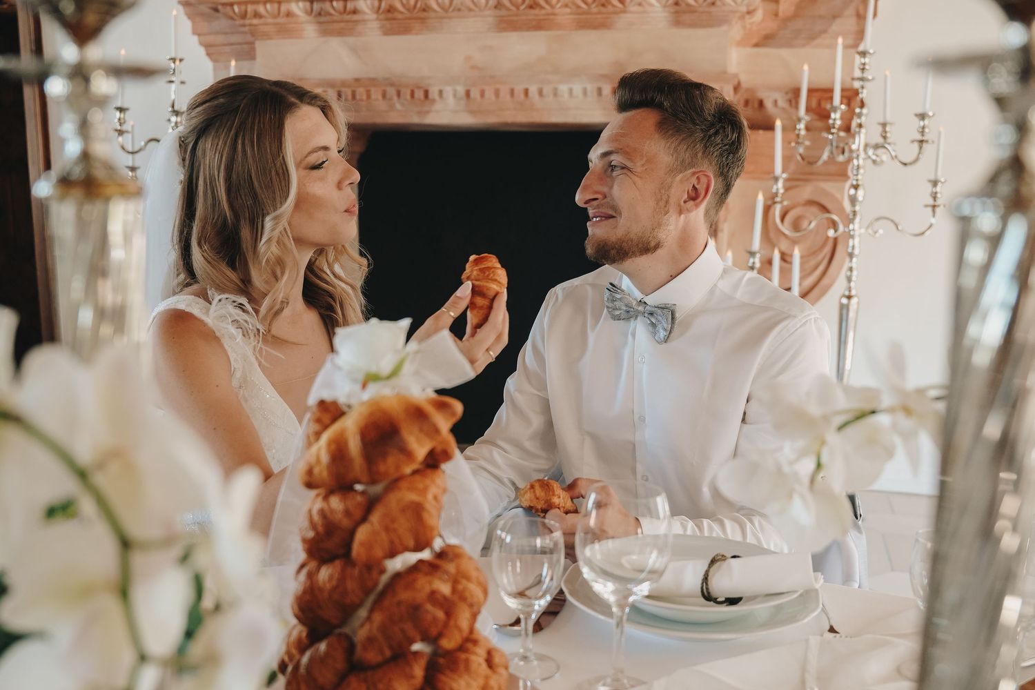 Bride and groom sharing a sweet moment at their wedding reception table with a croquembouche cake.