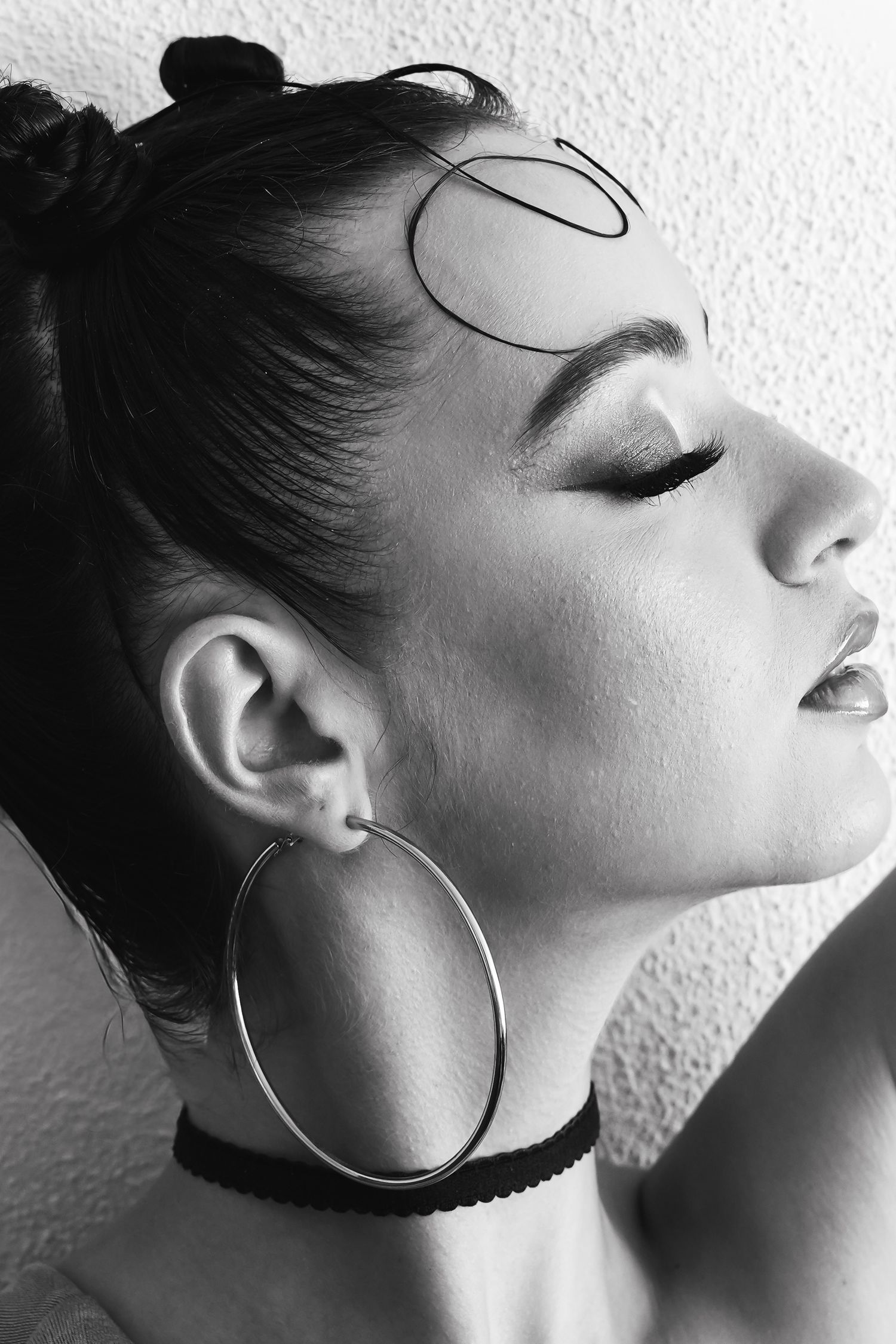 Black and white portrait of a woman with hoop earrings, choker necklace, and hair up, eyes closed.