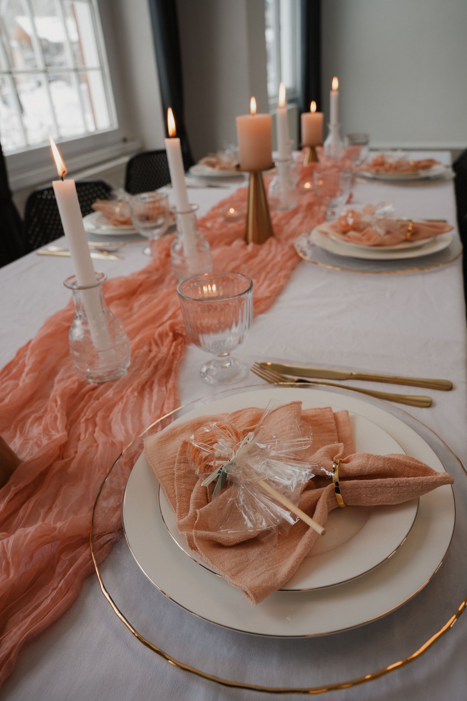 Elegant wedding table setting with peach chiffon runner, gold cutlery, white plates, lit candles, and decorative napkins.