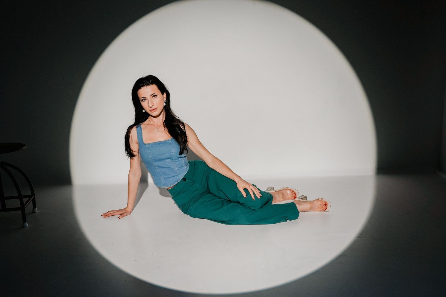 Woman in teal pants and blue top poses gracefully on floor against glowing circular backdrop.