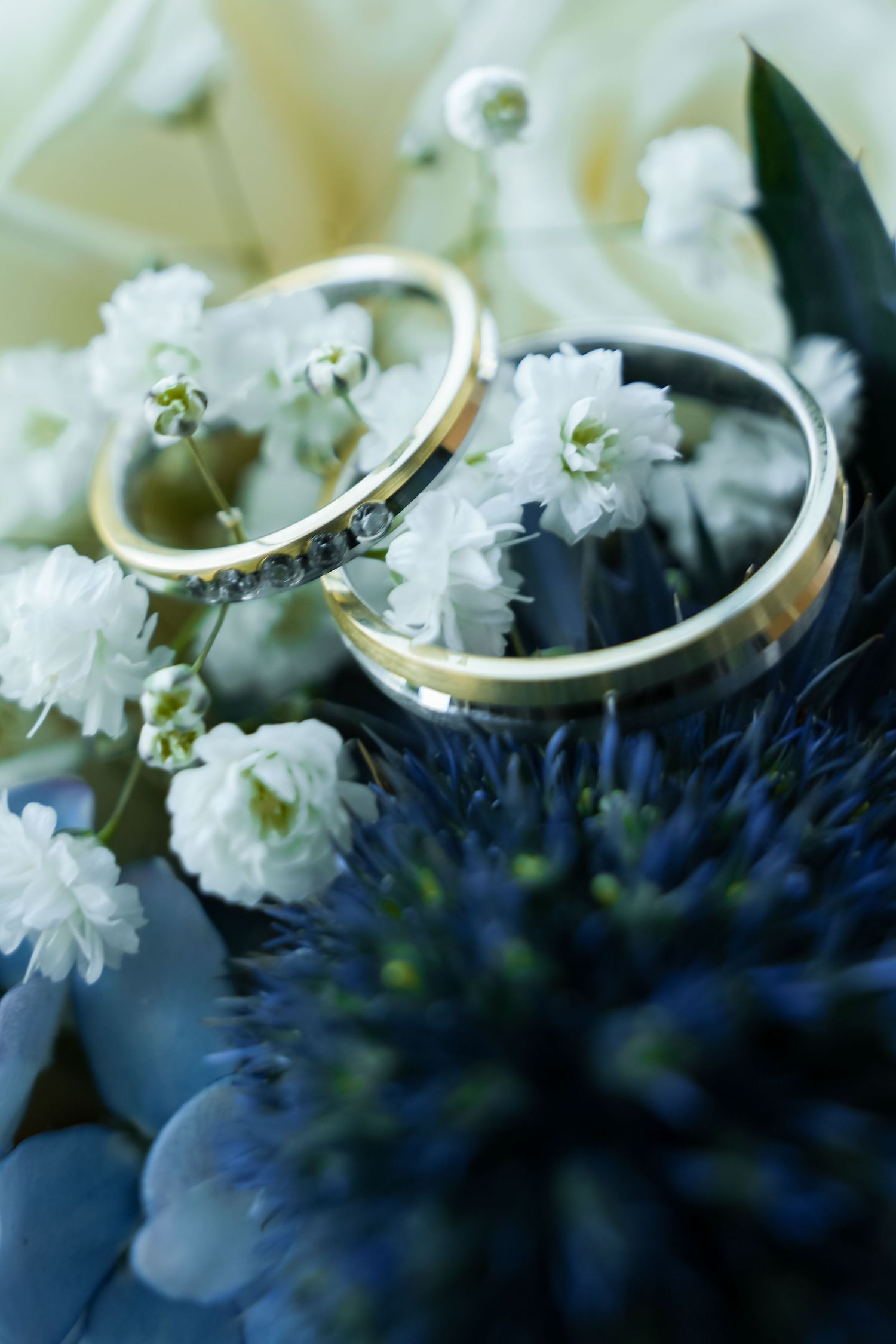 Two gold wedding rings resting on a bridal bouquet of white and blue flowers.