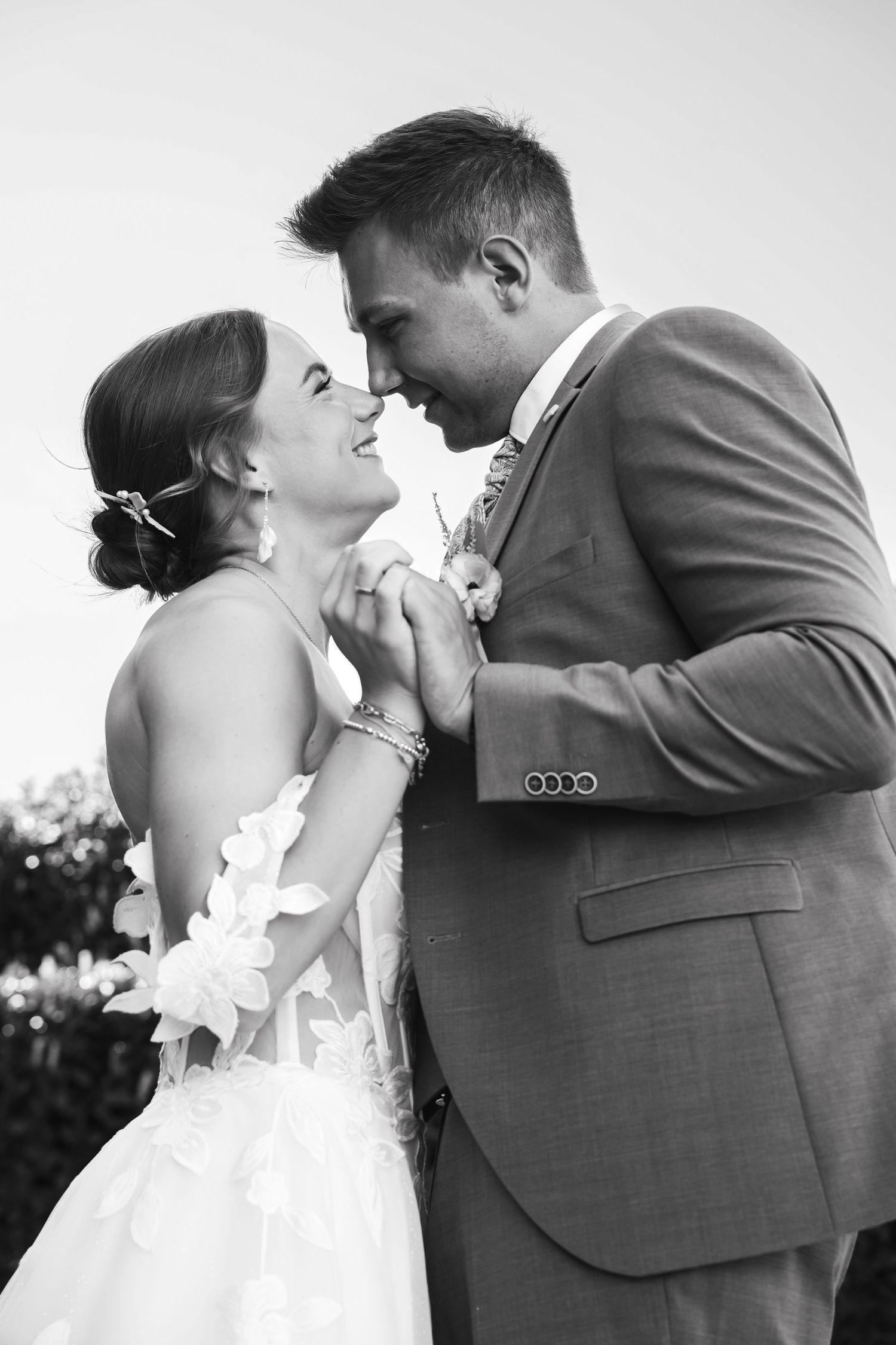 Black and white photo of a bride and groom sharing a romantic moment, nearly kissing at their wedding.